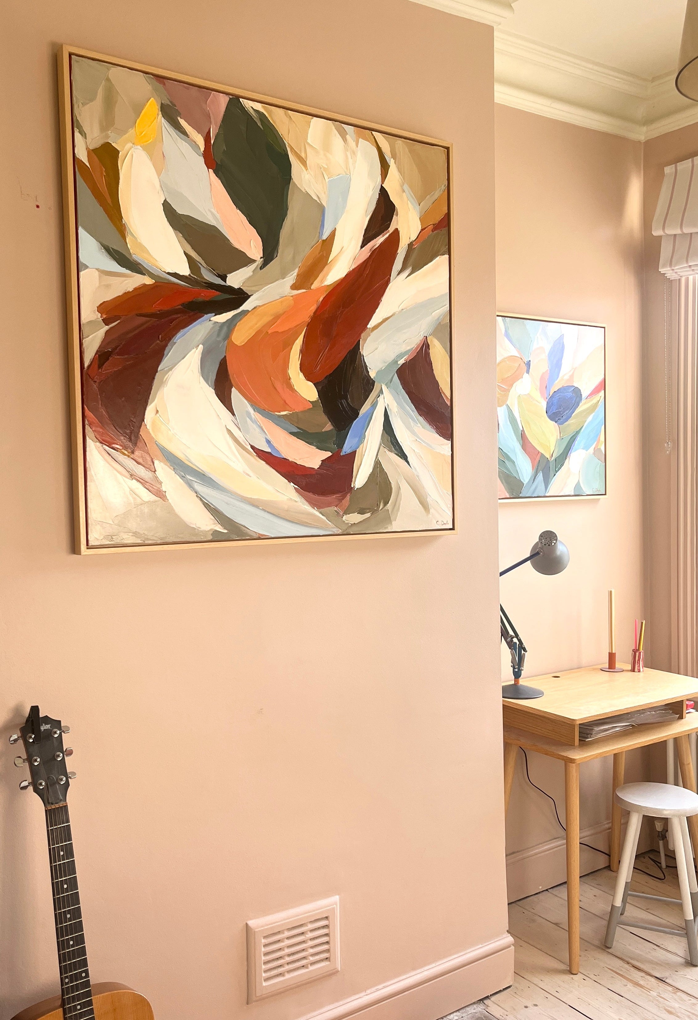 Abstract art on a wall with a guitar and desk in the background