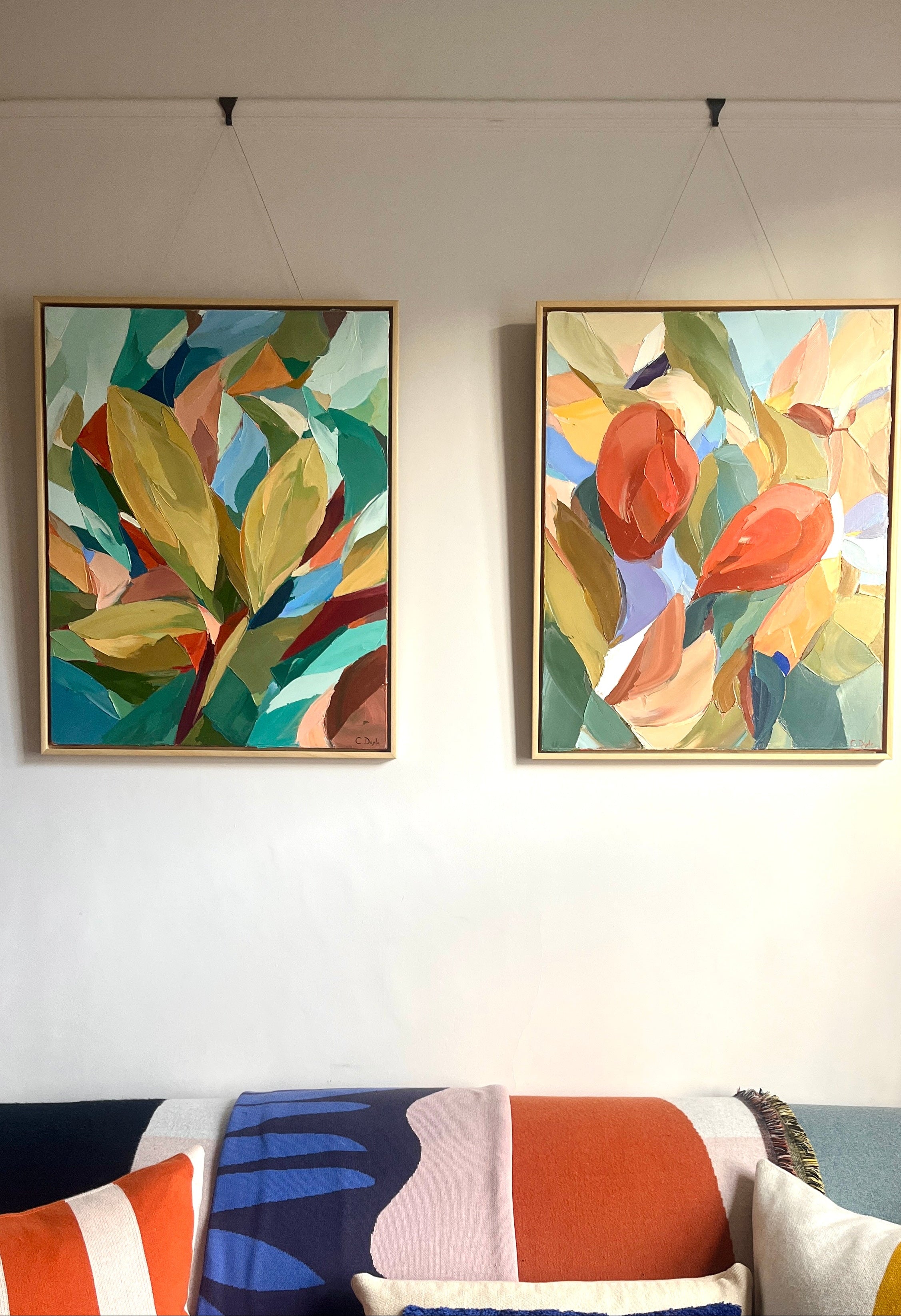 Two colorful abstract paintings on a wall above a sofa with a patterned throw.
