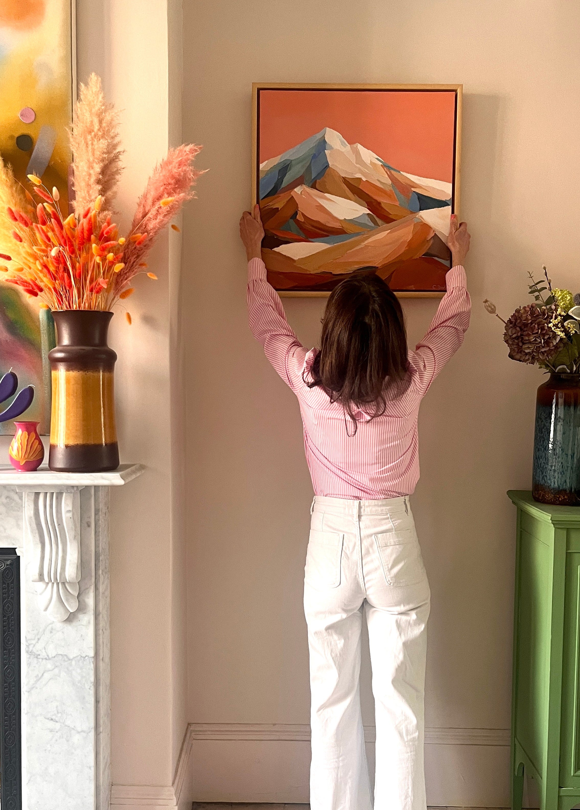 Image of woman hanging piece of art on wall
