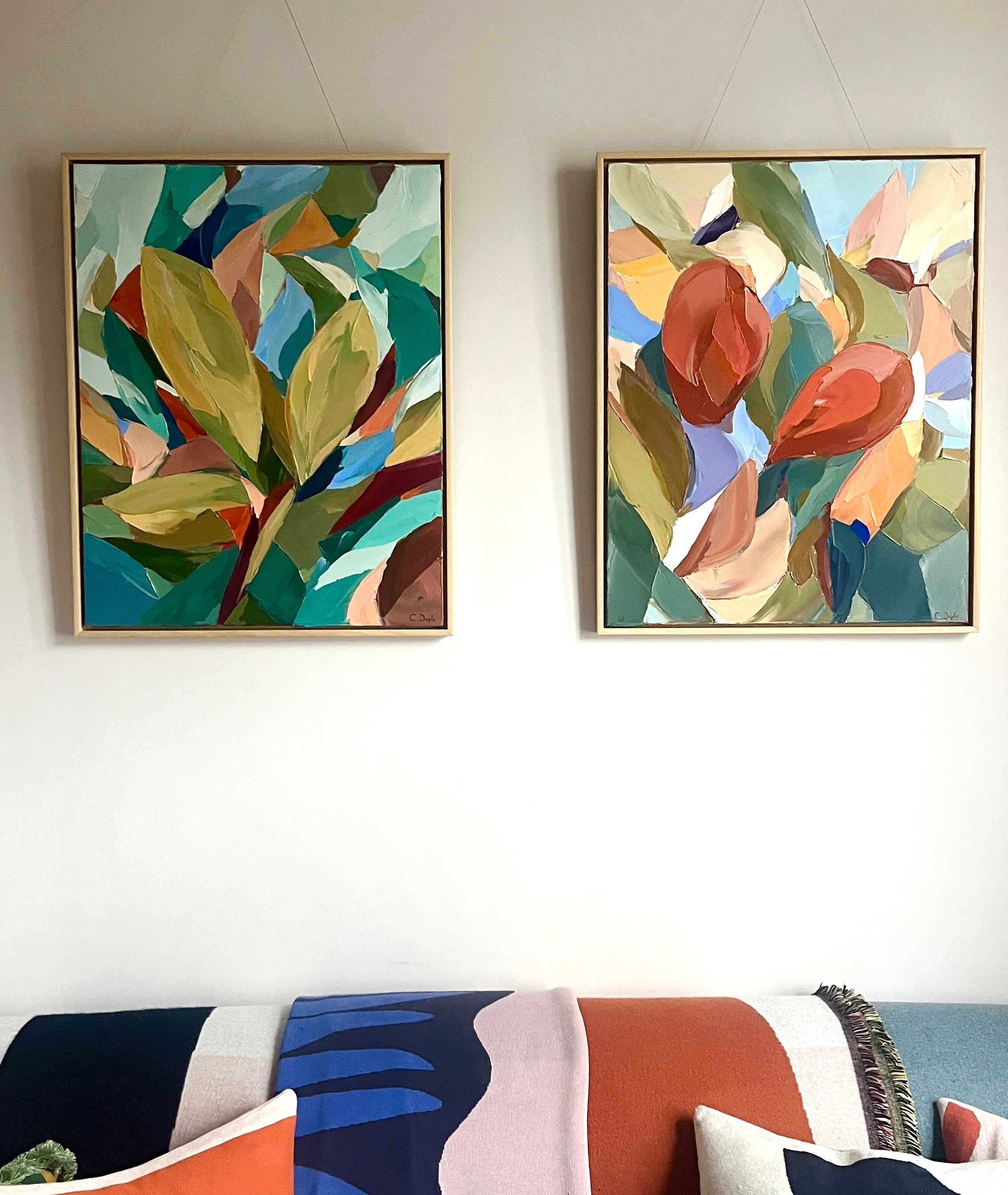 Two abstract art pieces on a wall above a colorful sofa.