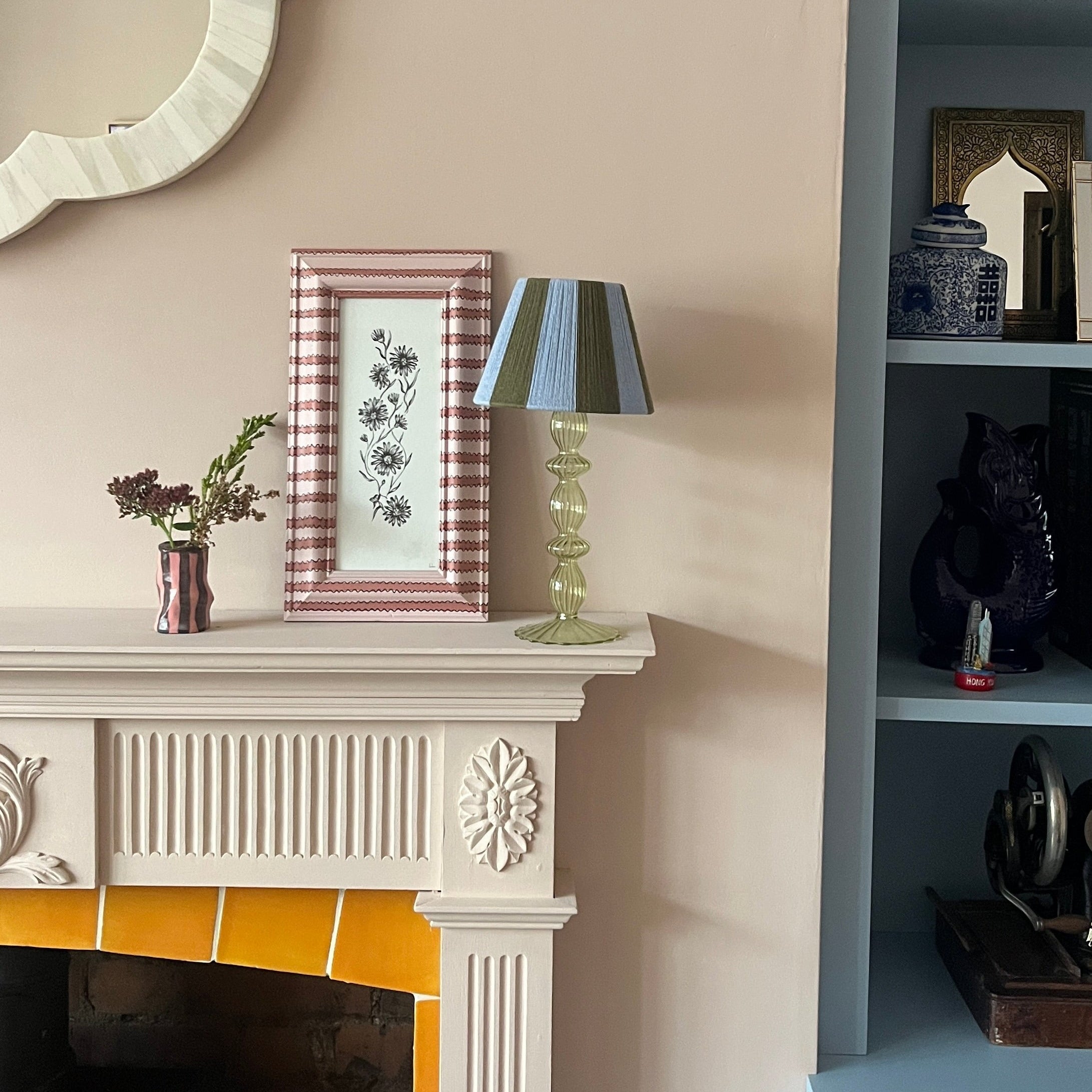 Decorative fireplace with mantel, mirror, and shelves against a beige wall.