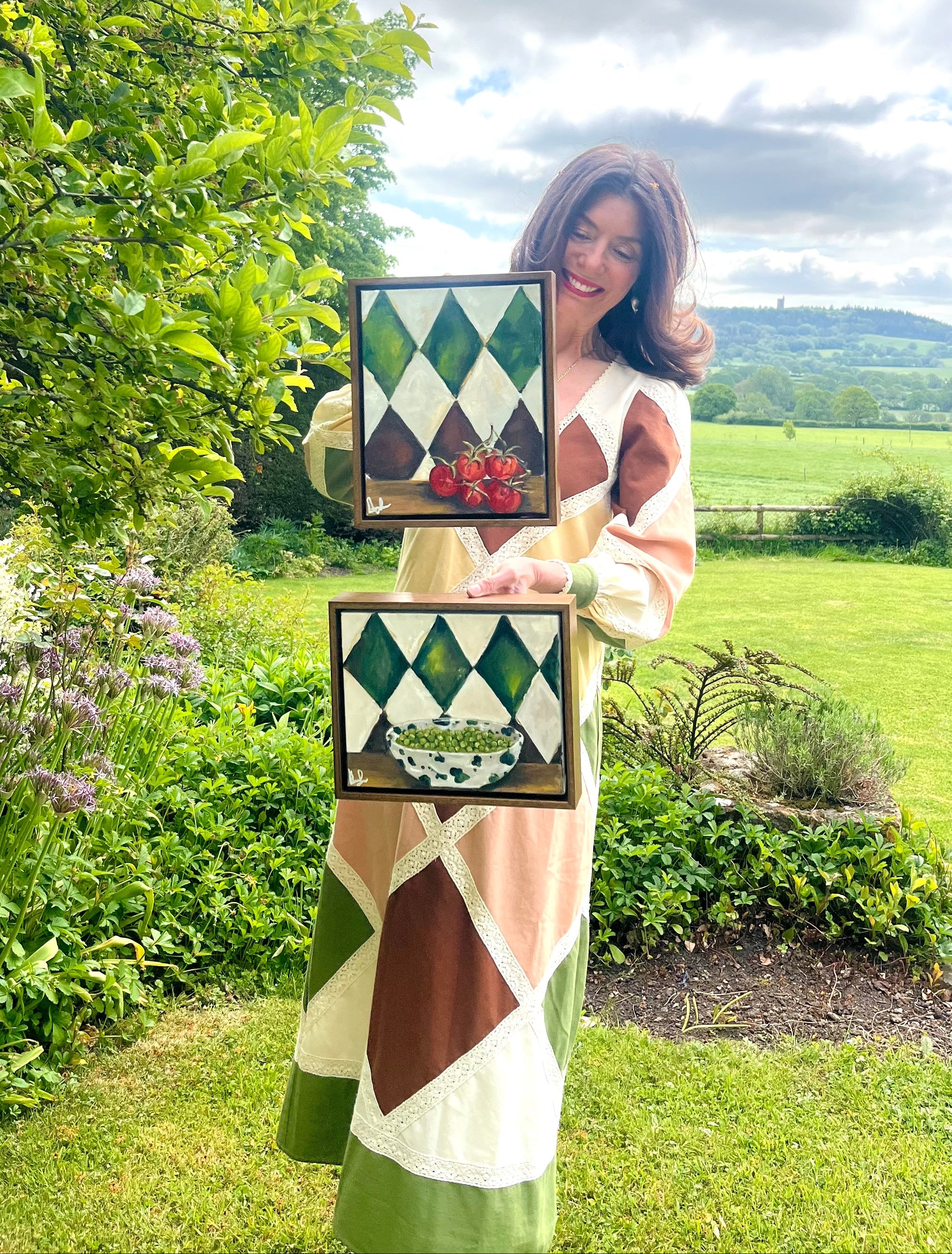 Woman holding two framed still life images in a garden setting