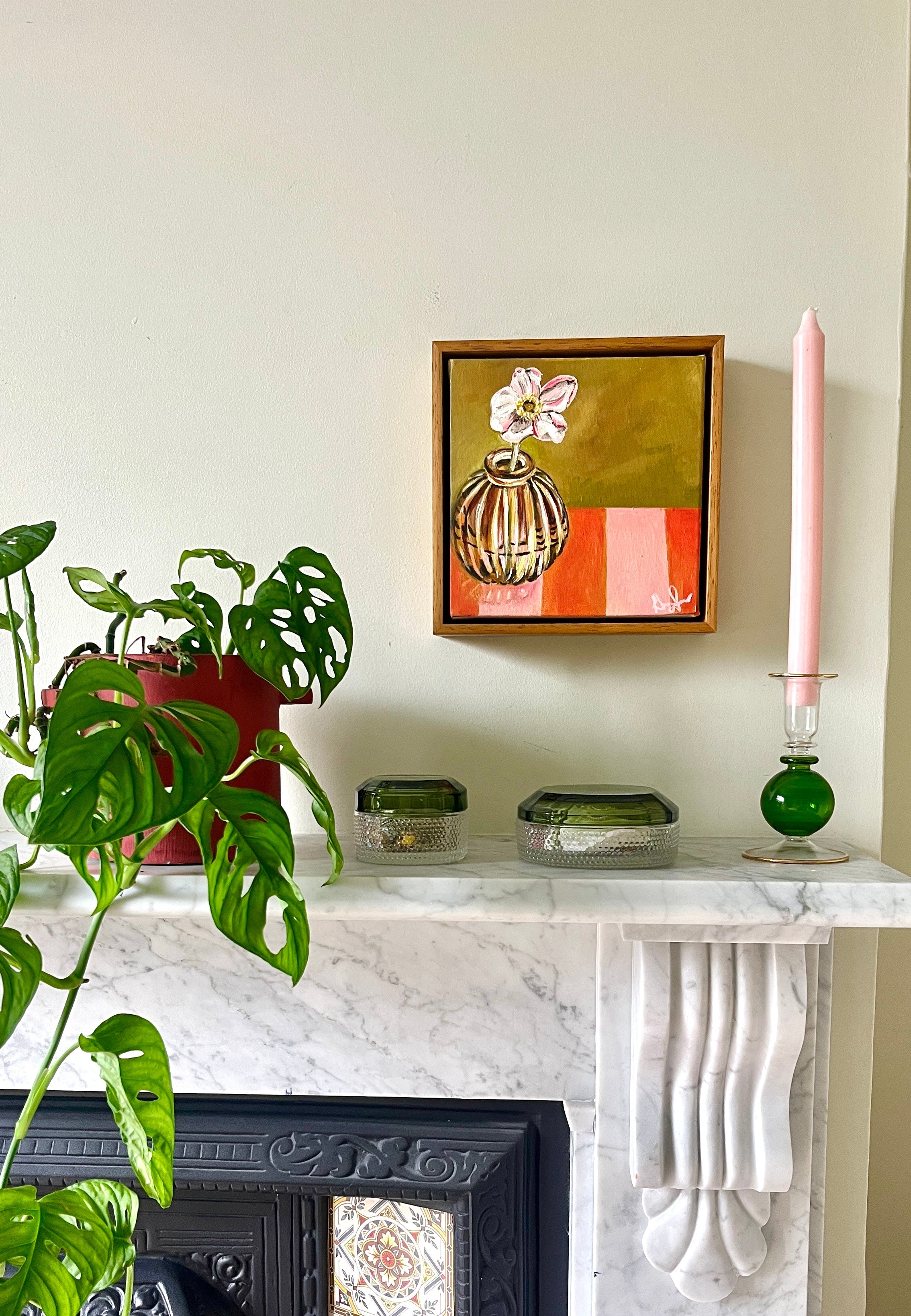 Decorative mantelpiece with a plant, candle, and framed Emma Gurner artwork.