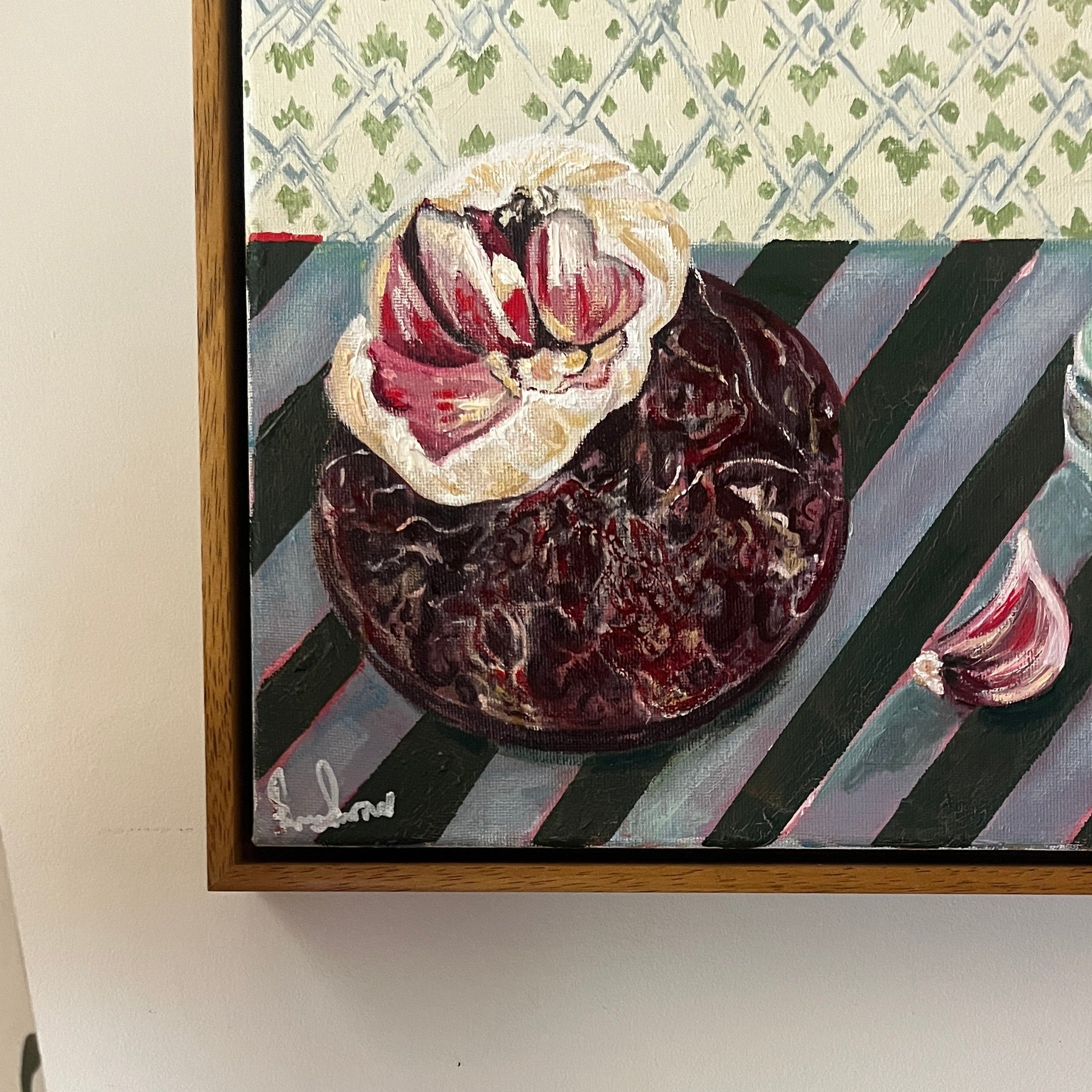 Framed artwork with still life of garlic on a plate sat on a striped tablecloth