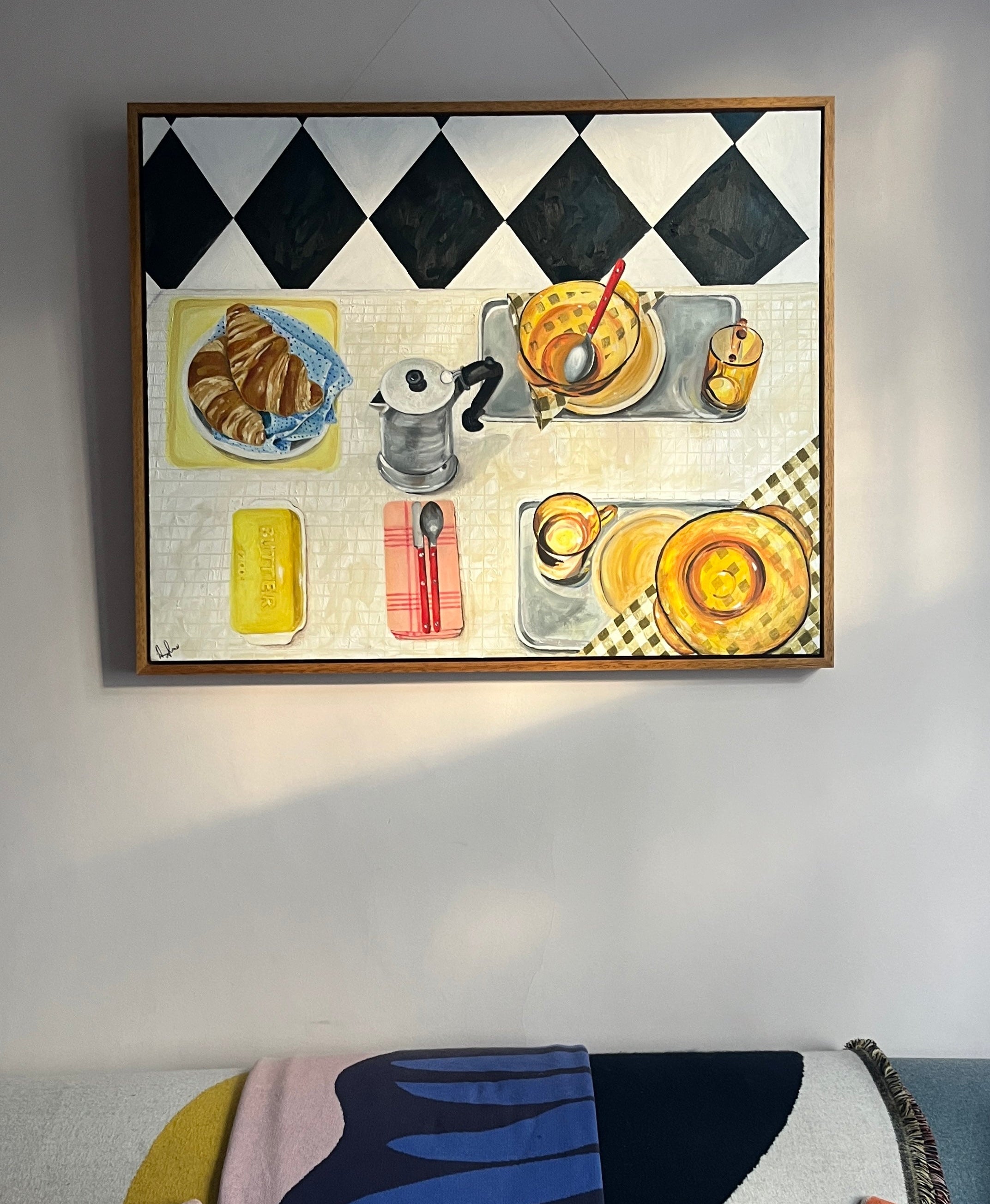 Framed artwork of a still life scene with food and drinks on a checkered tablecloth.