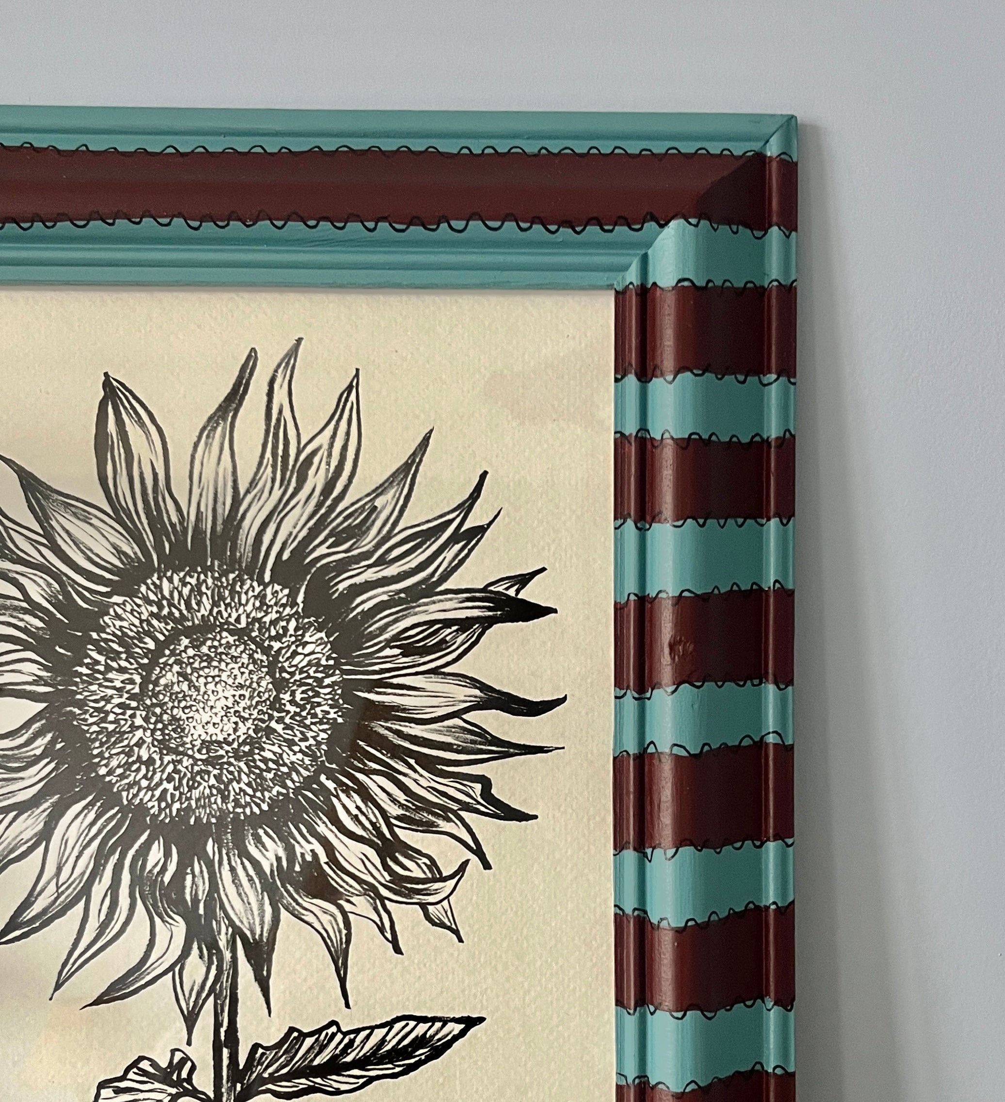 Framed artwork of a sunflower with striped border on a gray wall