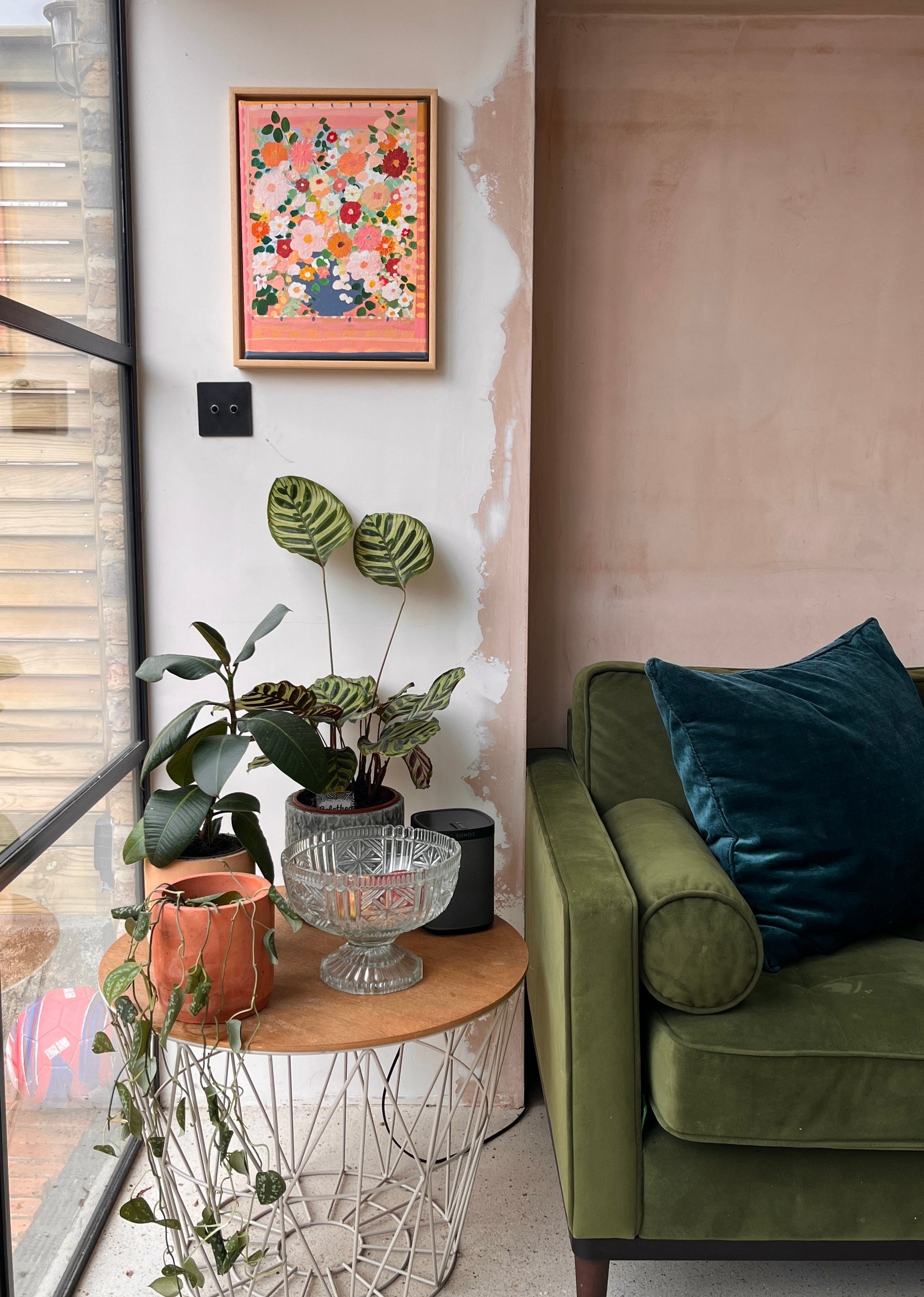 Living room with green sofa, decorative plants, and a wall art piece.