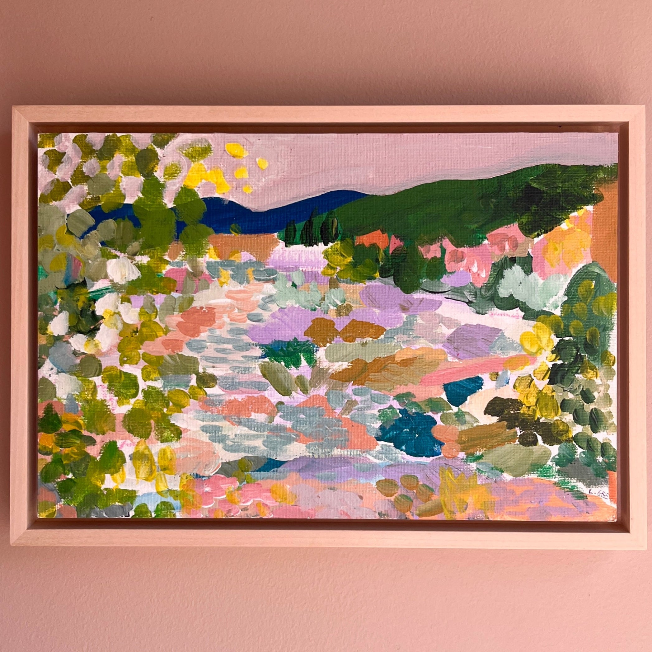 Colourful artworks framed in a light wood on a peach wall.