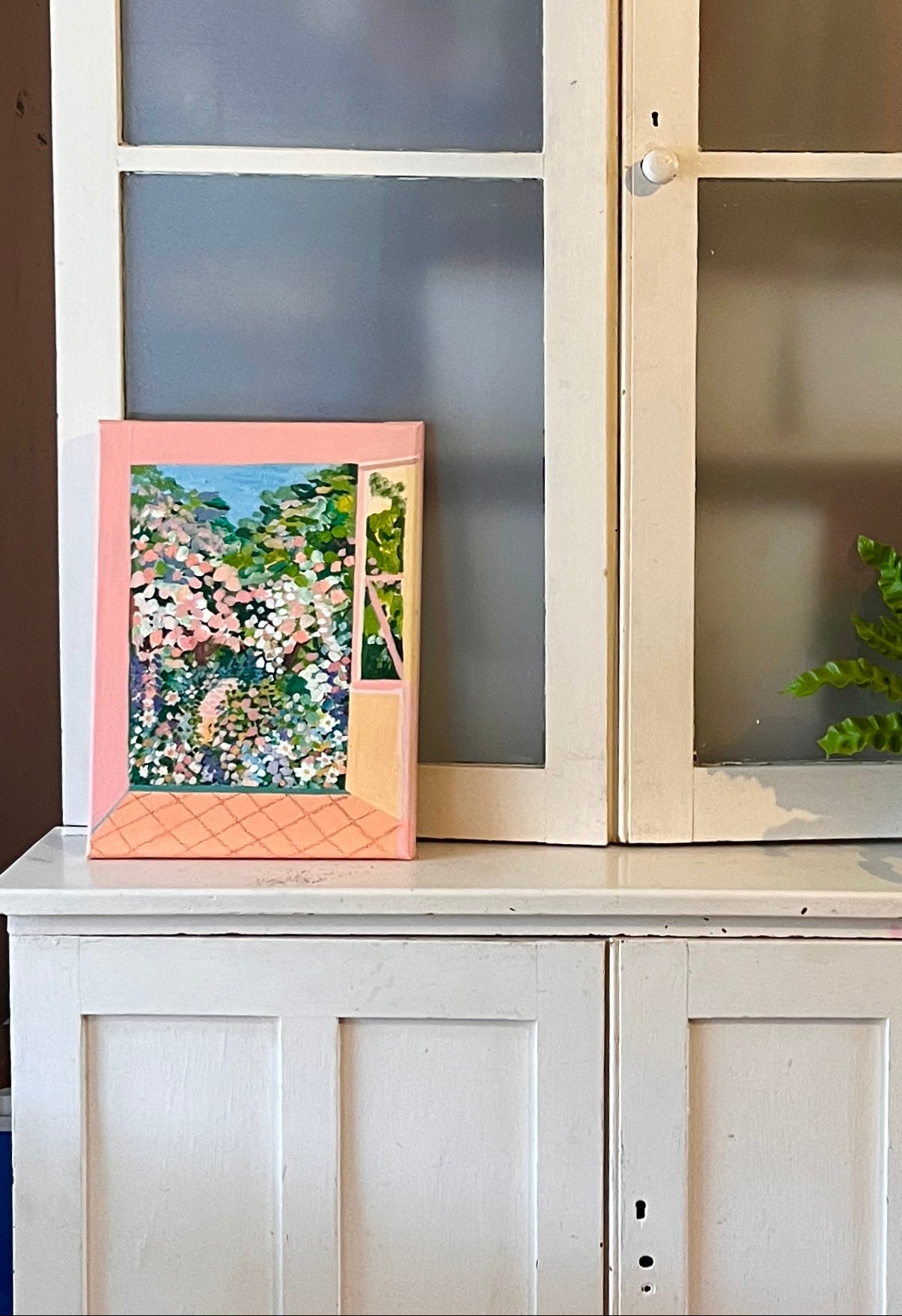 Pink framed picture on a white cabinet with glass doors