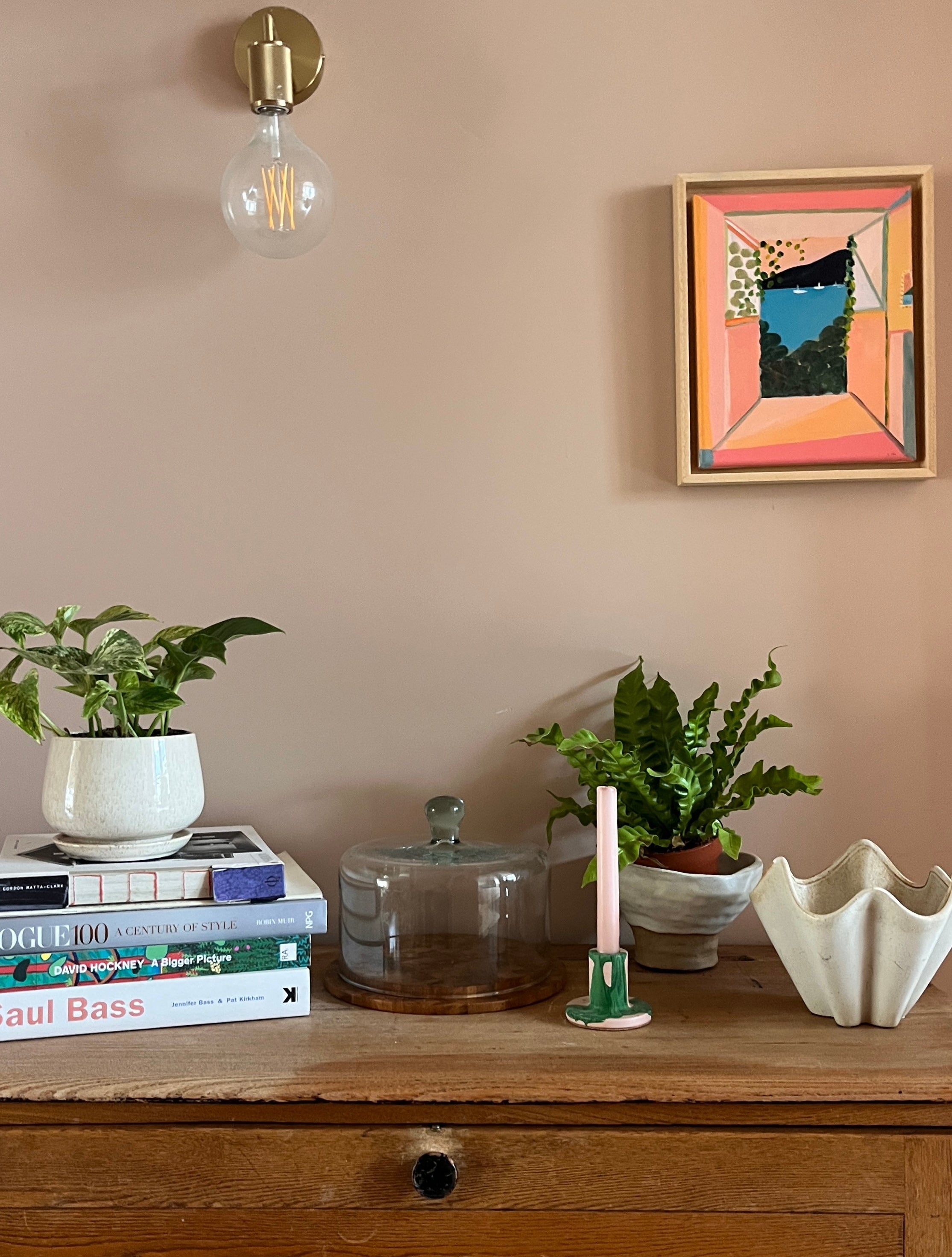 Decorative setup with books, plants, and a small sculpture on a wooden surface against a beige wall.