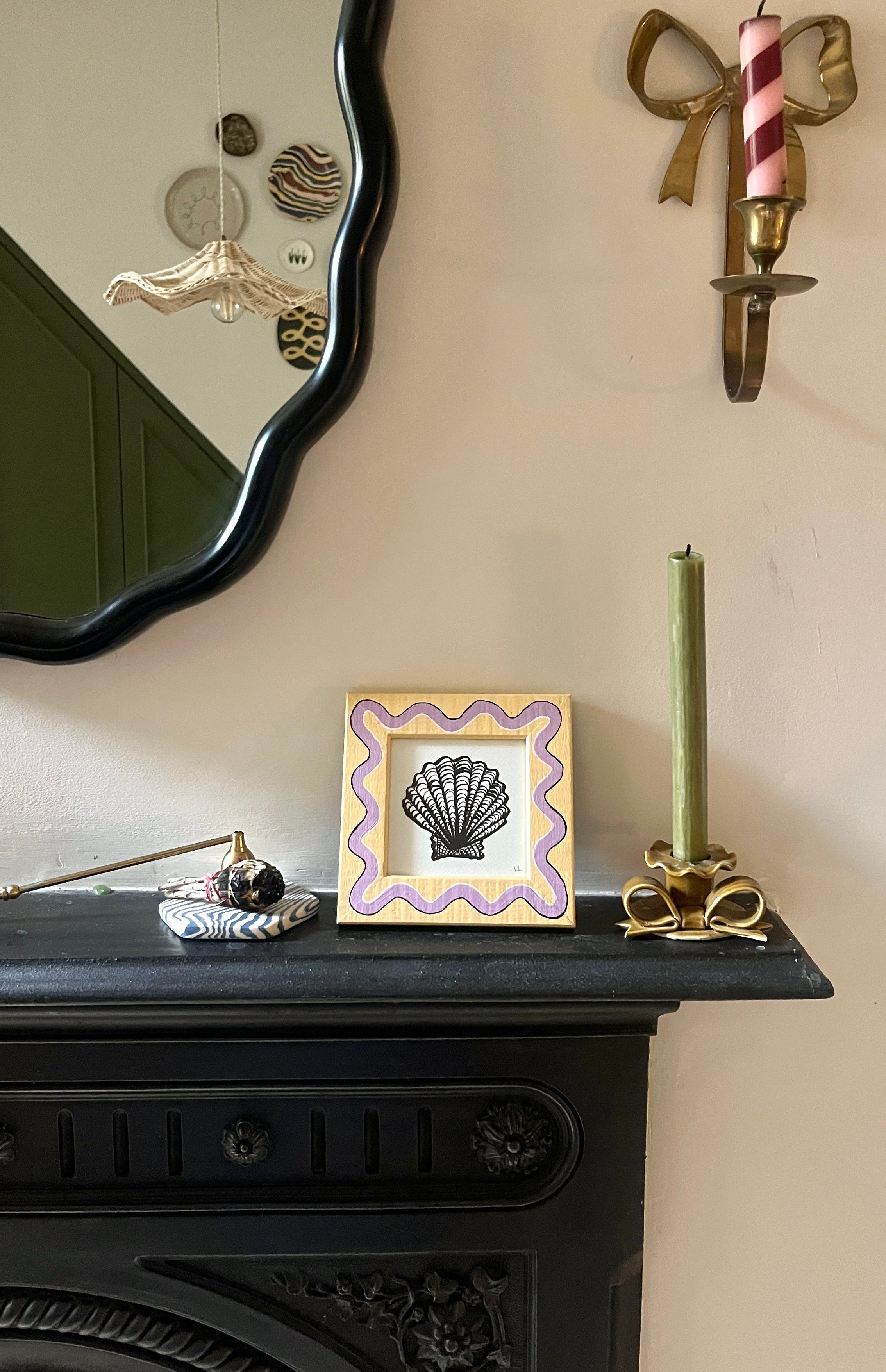 Decorative mantelpiece with a mirror, candle, and framed picture on a beige wall.