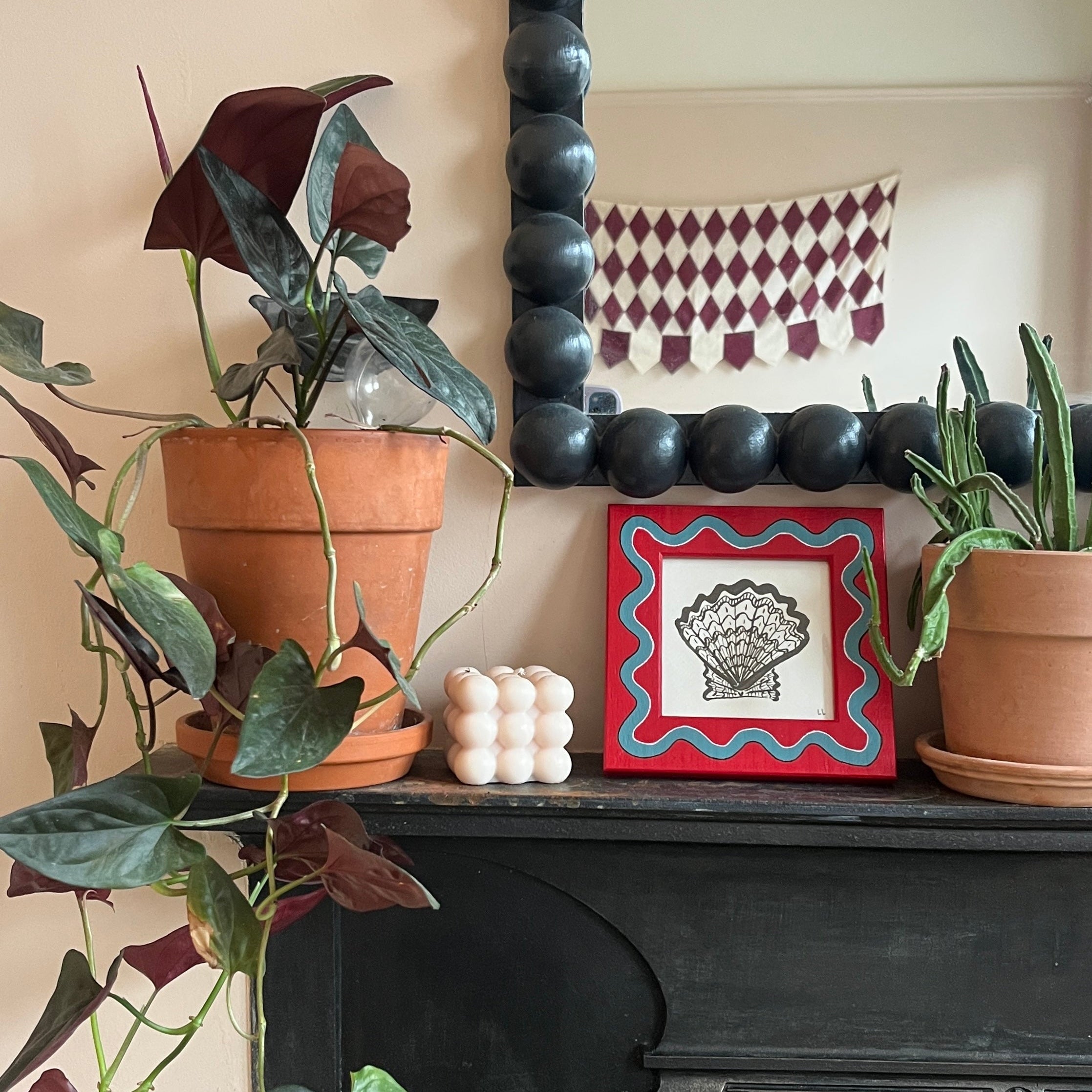 Decorative fireplace with plants and a framed picture on a mantel.