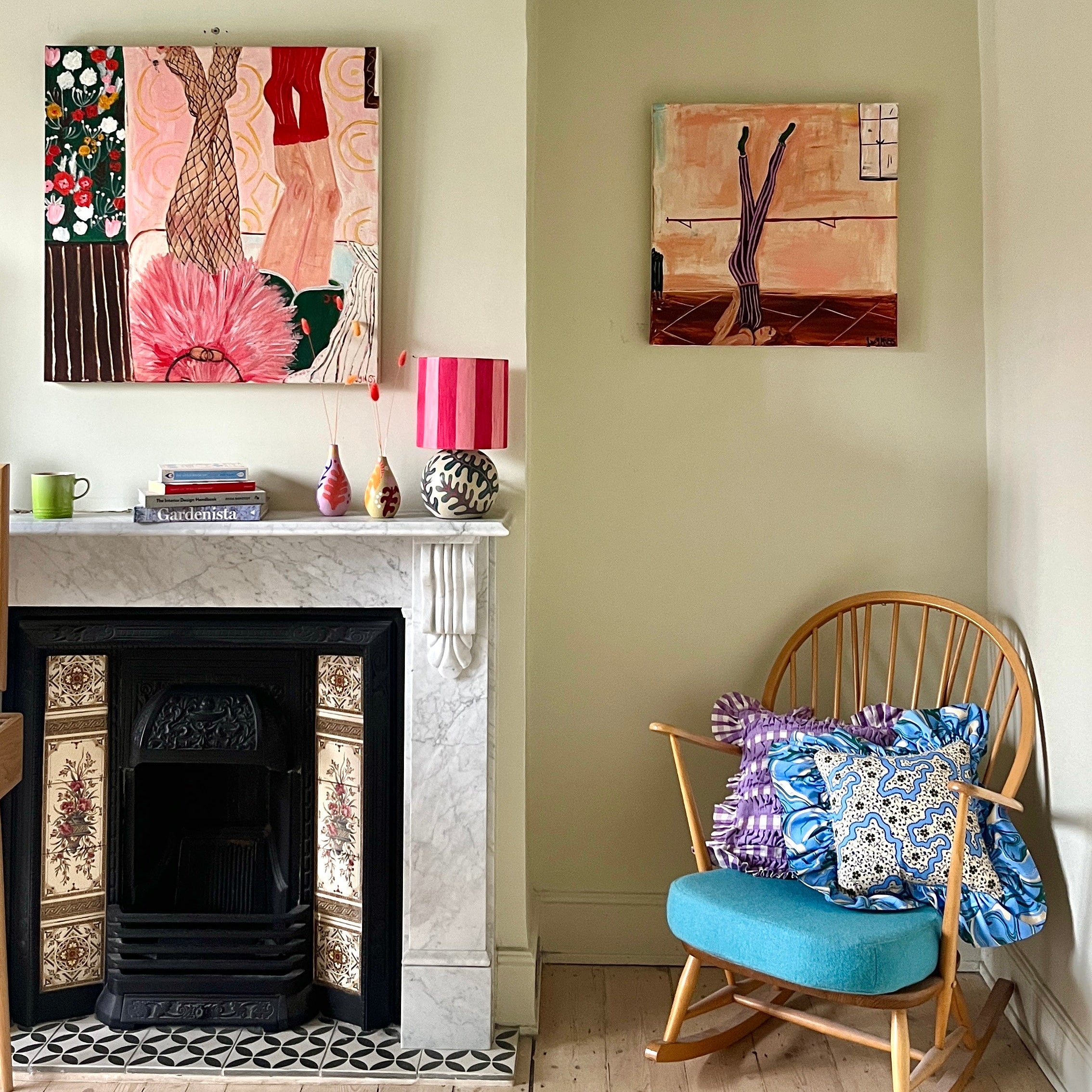 Picture of a fireplace with two paintings either side and a wooden rocking chair.