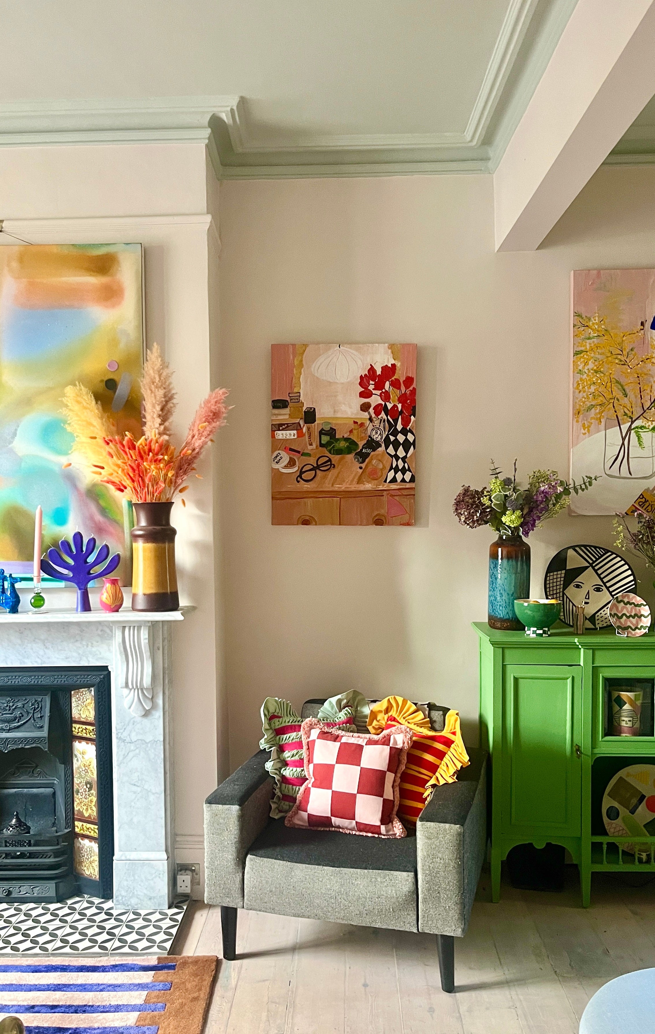 Living room scene of chair with painting above it sat between green unit and fireplace.