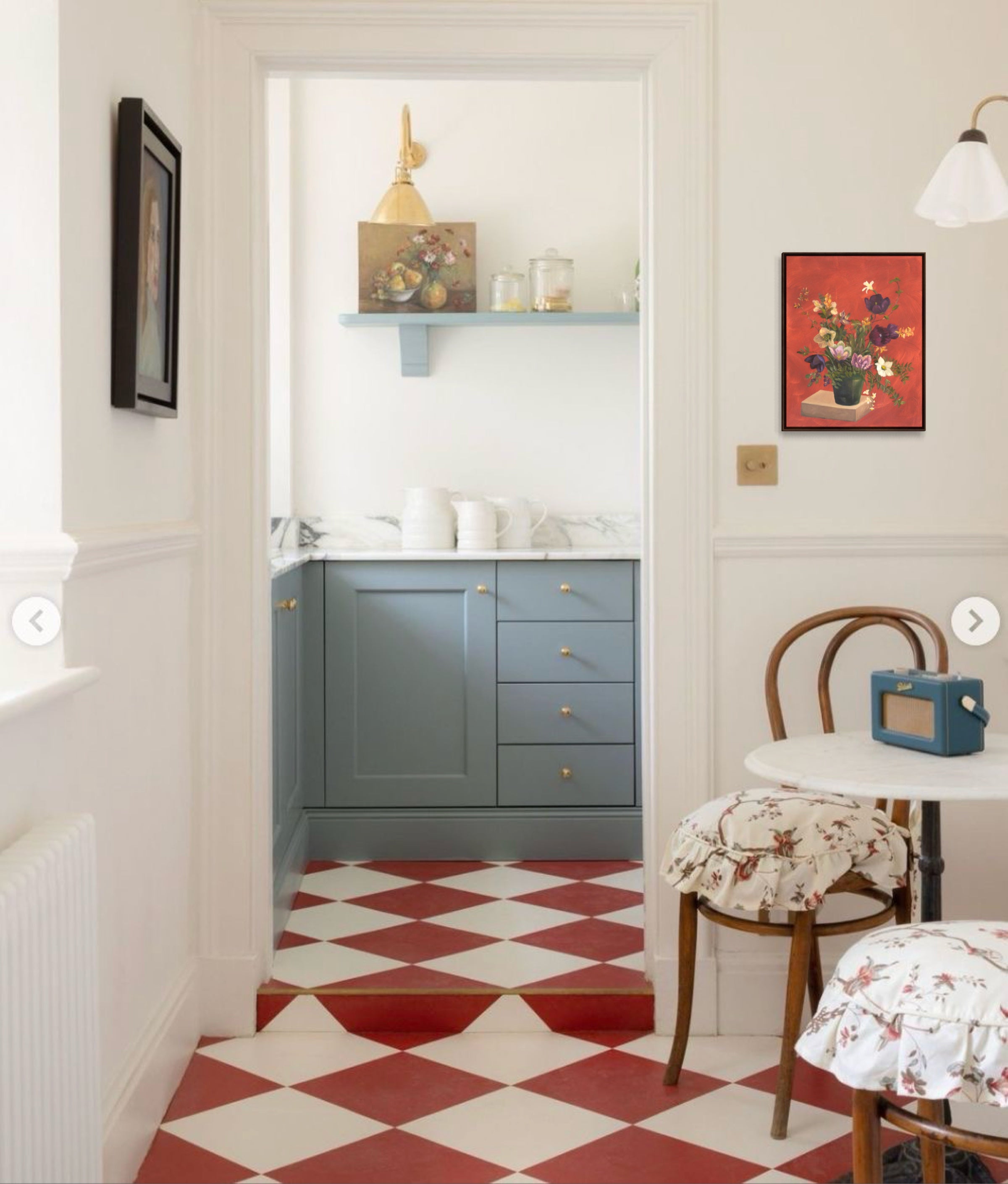 Kitchen with red and white checkered floor, blue cabinets, and a chair with a floral cushion.