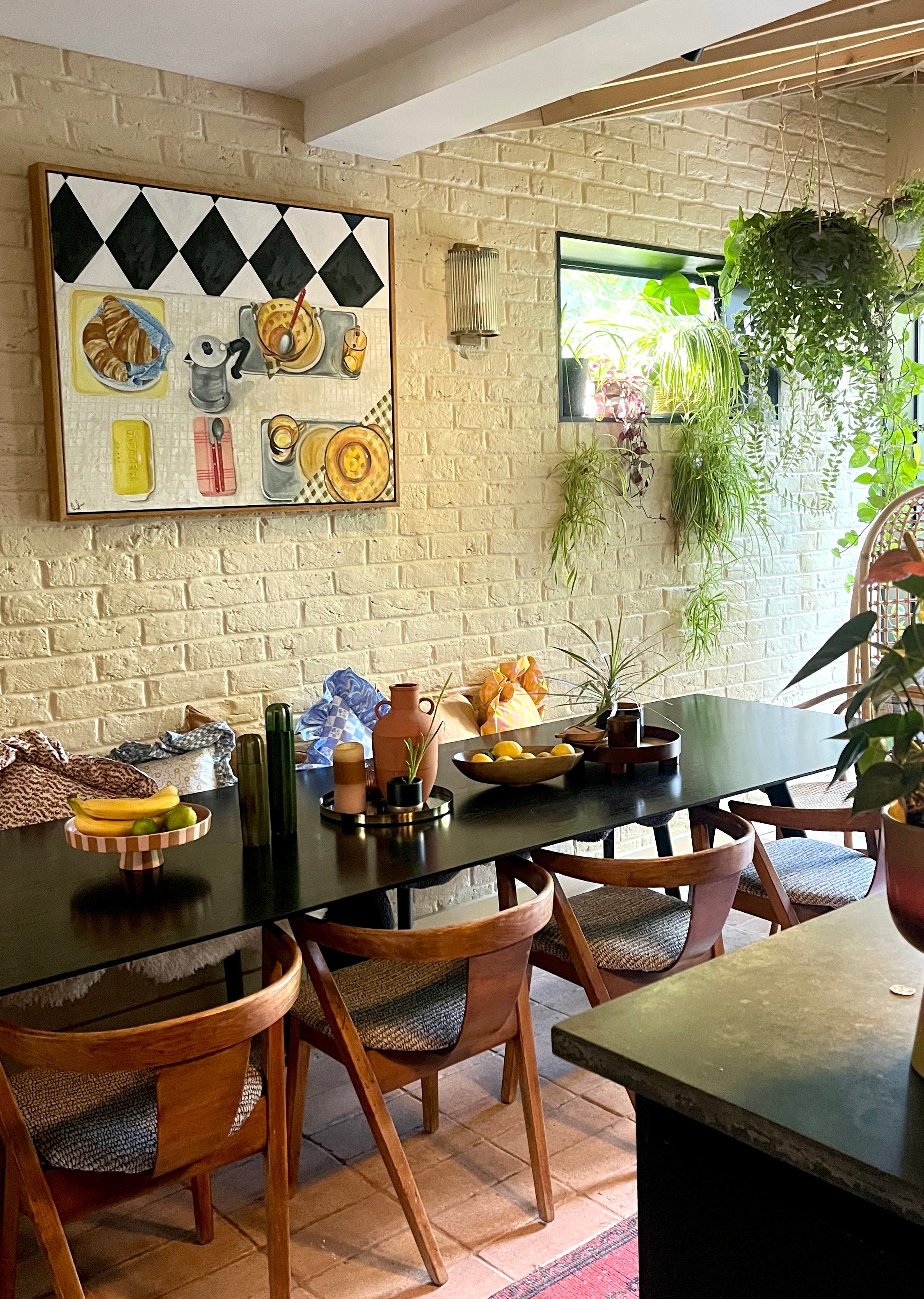 Dining room with a brick wall, framed artwork by Emma Gurner , and wooden chairs