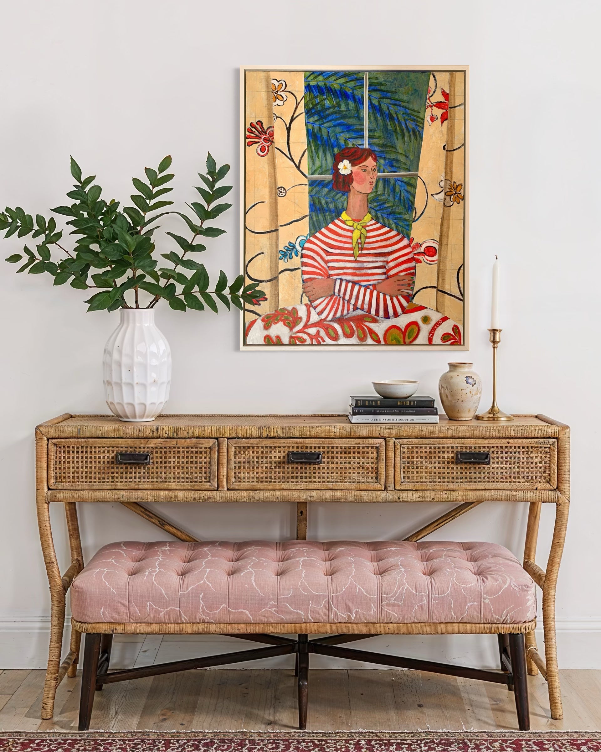 Console table with a pink bench, vase, and framed artwork on a white wall.
