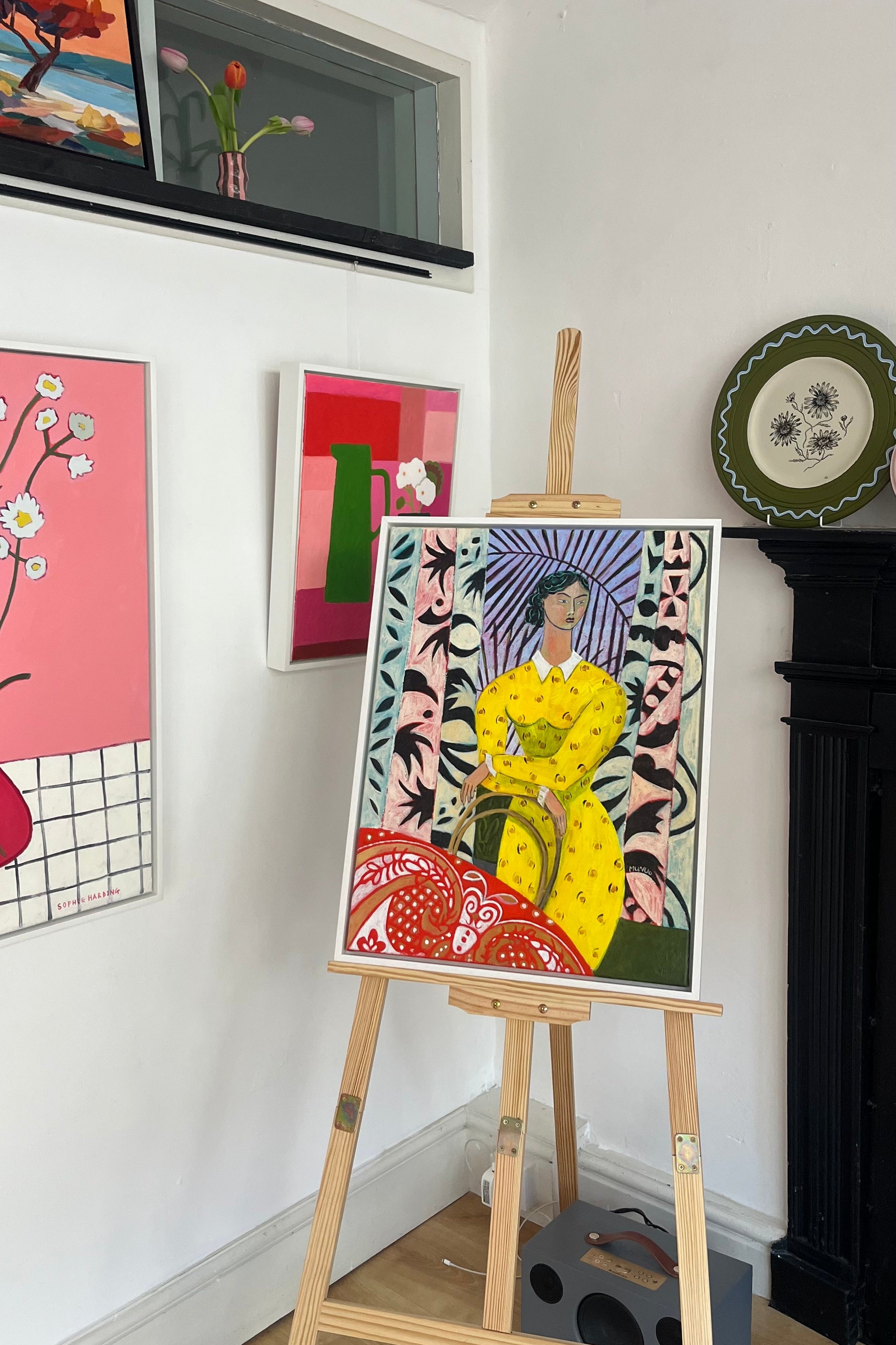Artistic display with a colorful painting on an easel against a white wall.