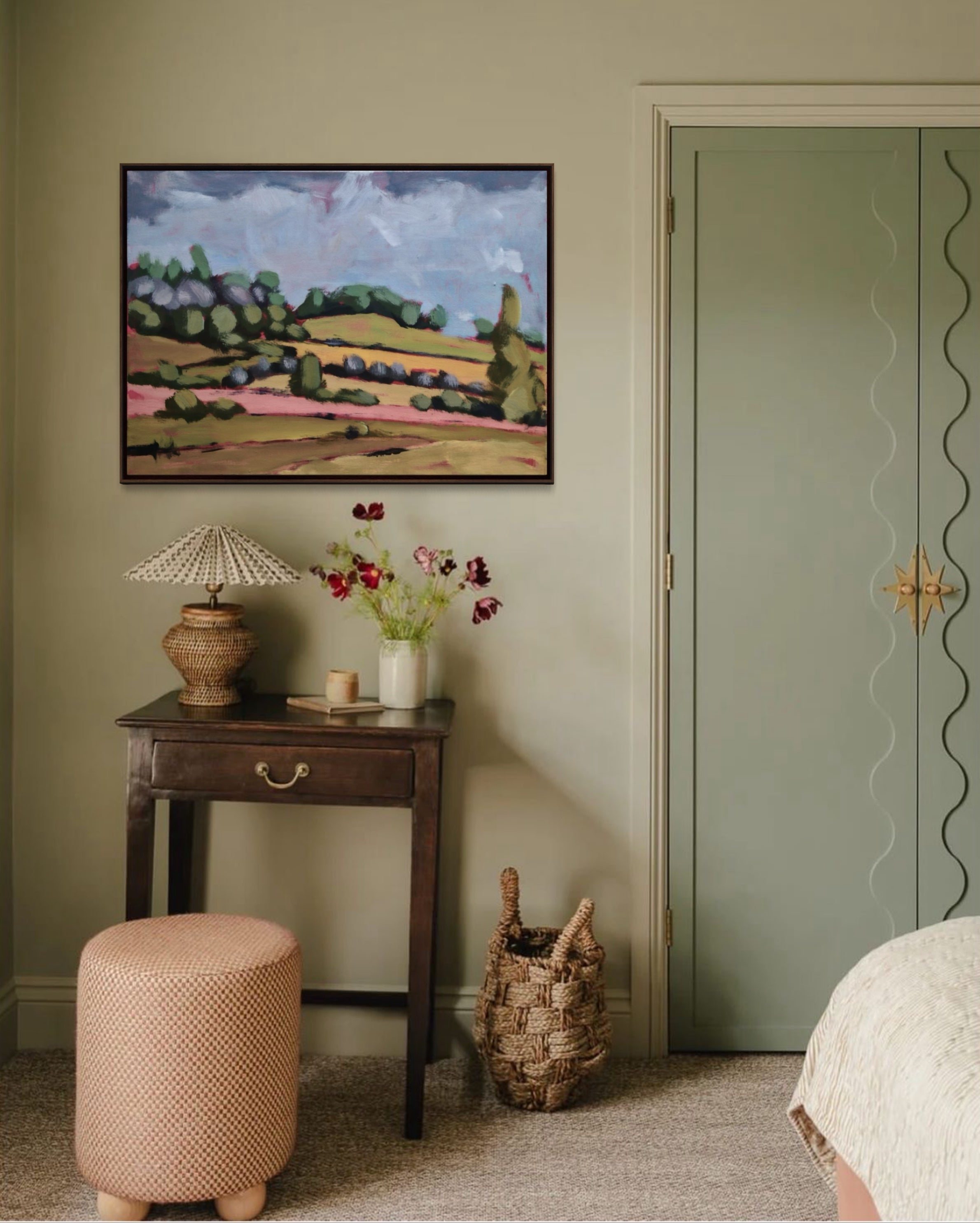 Room interior with a painting on the wall, table with lamp and flowers, and a door.