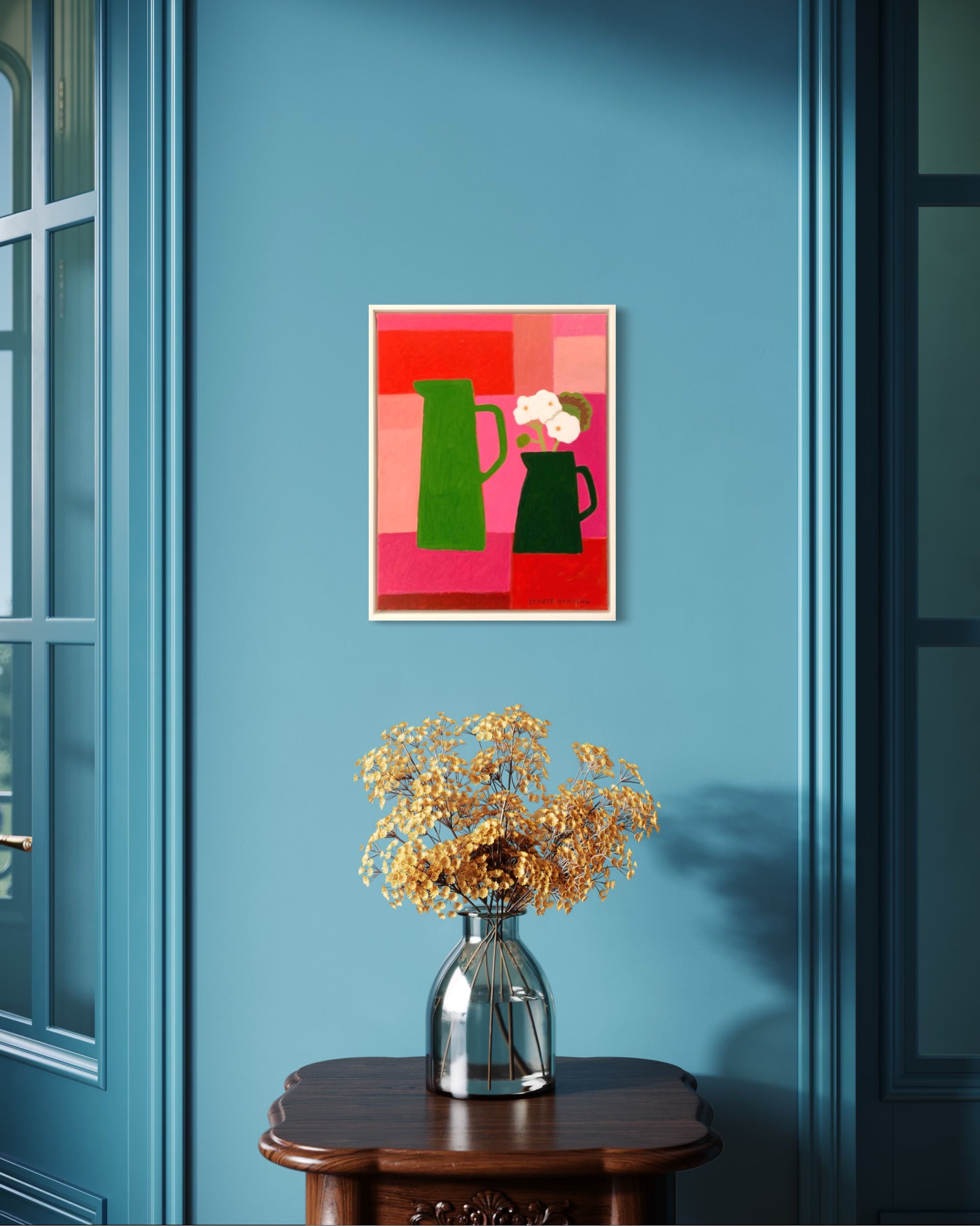 Colorful abstract painting on a blue wall with a vase of flowers on a table.
