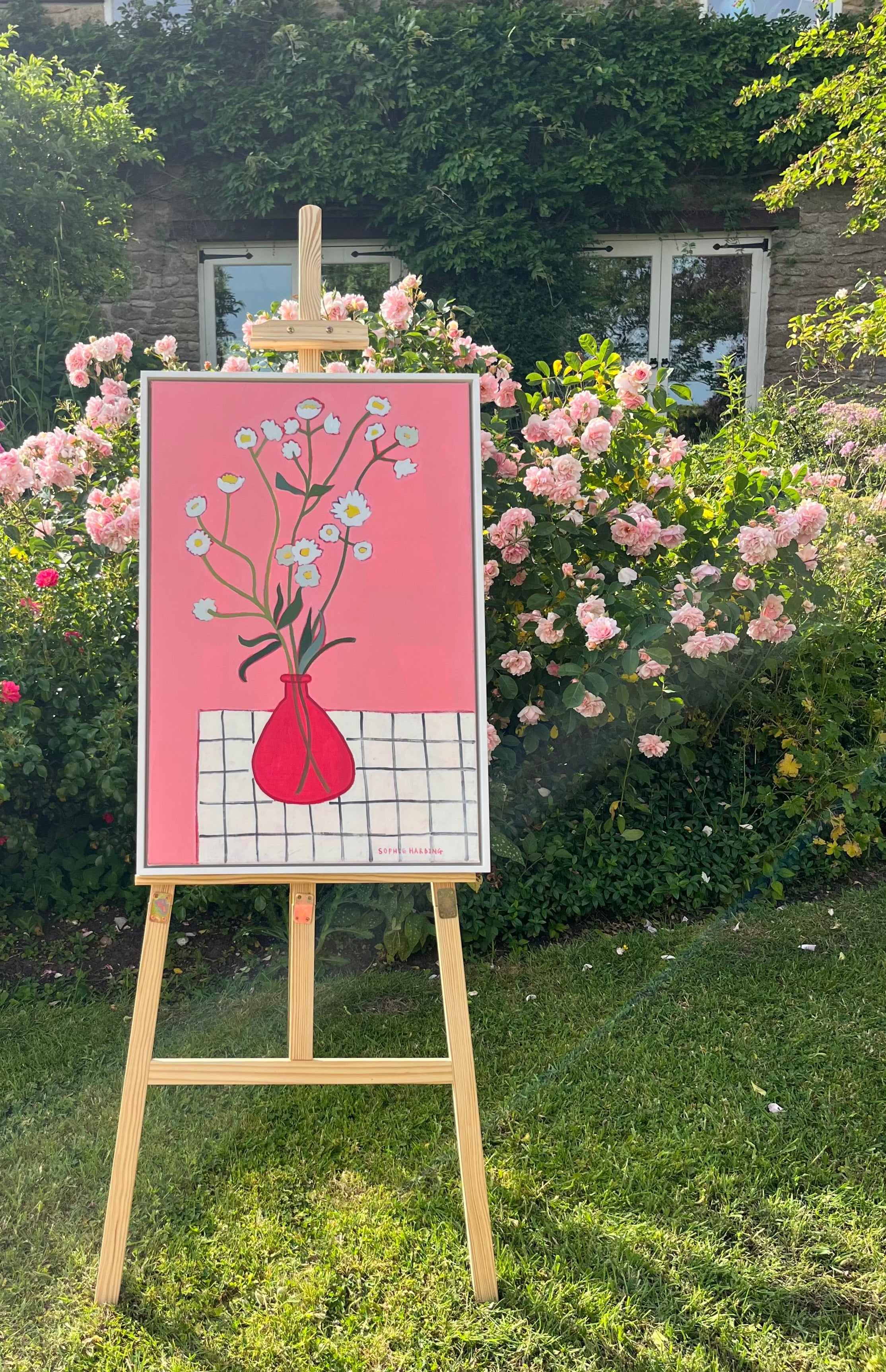 Painting of a red vase with flowers on an easel outdoors
