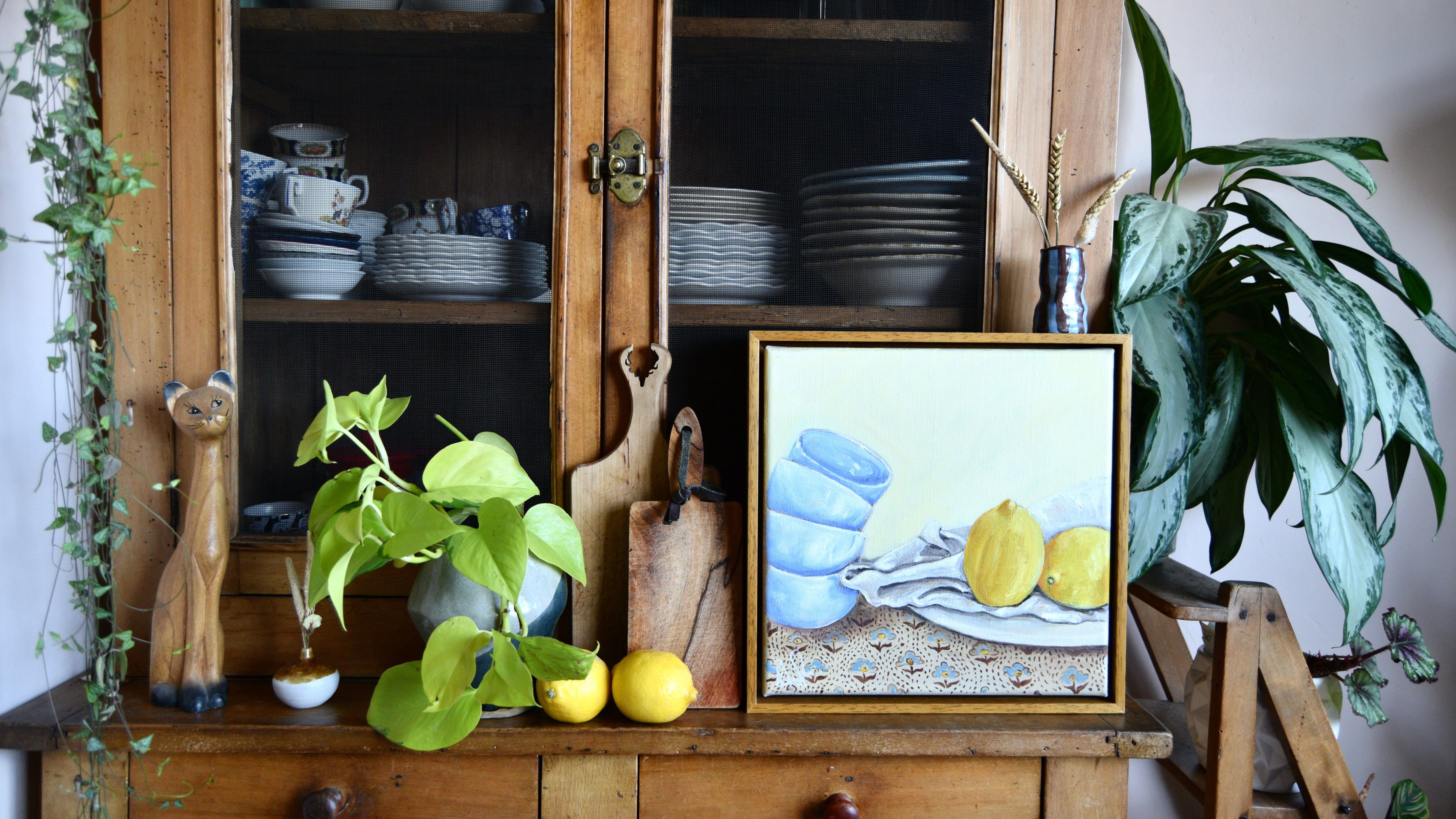 Original oil painting Stacked – With Lemons by Emma Gurner, showing stacked teacups and bright lemons in a playful naïve style, framed in an oak tray frame