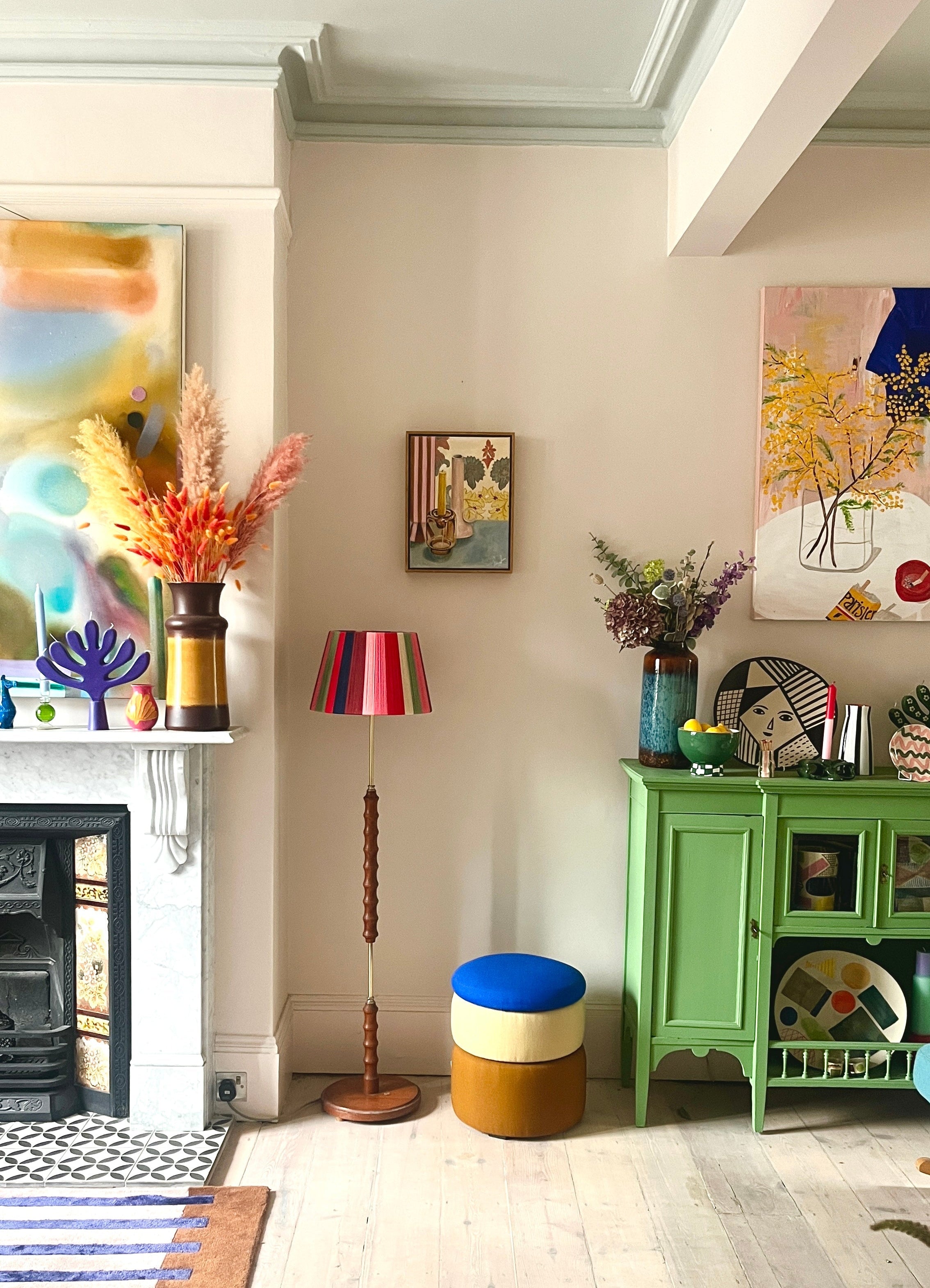 Living room with a green cabinet, colorful stool, and decorative items including framed still life by Emma Gurner
