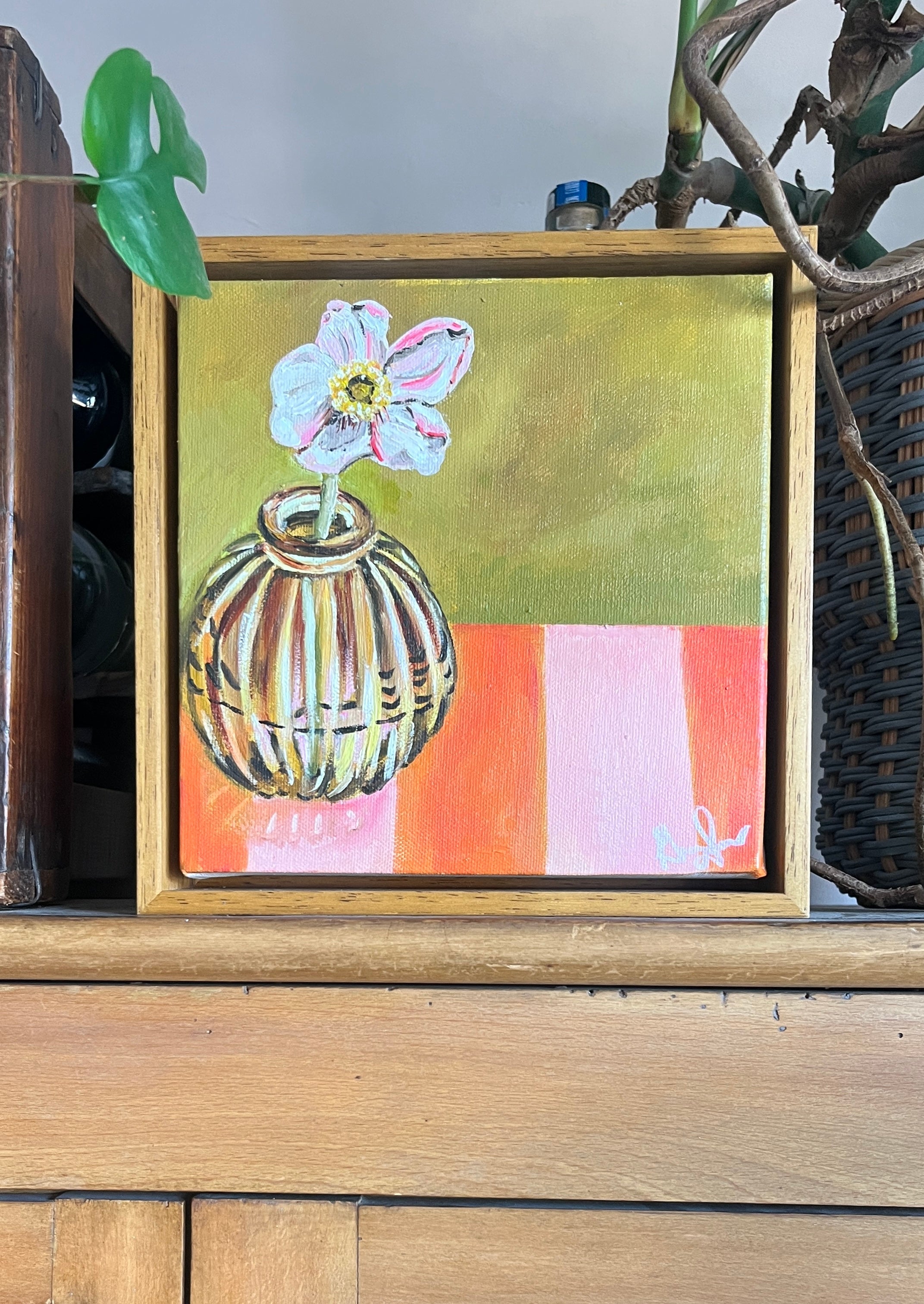 Small painting of a welsh flower in a vase on a striped background, framed in a wooden box.
