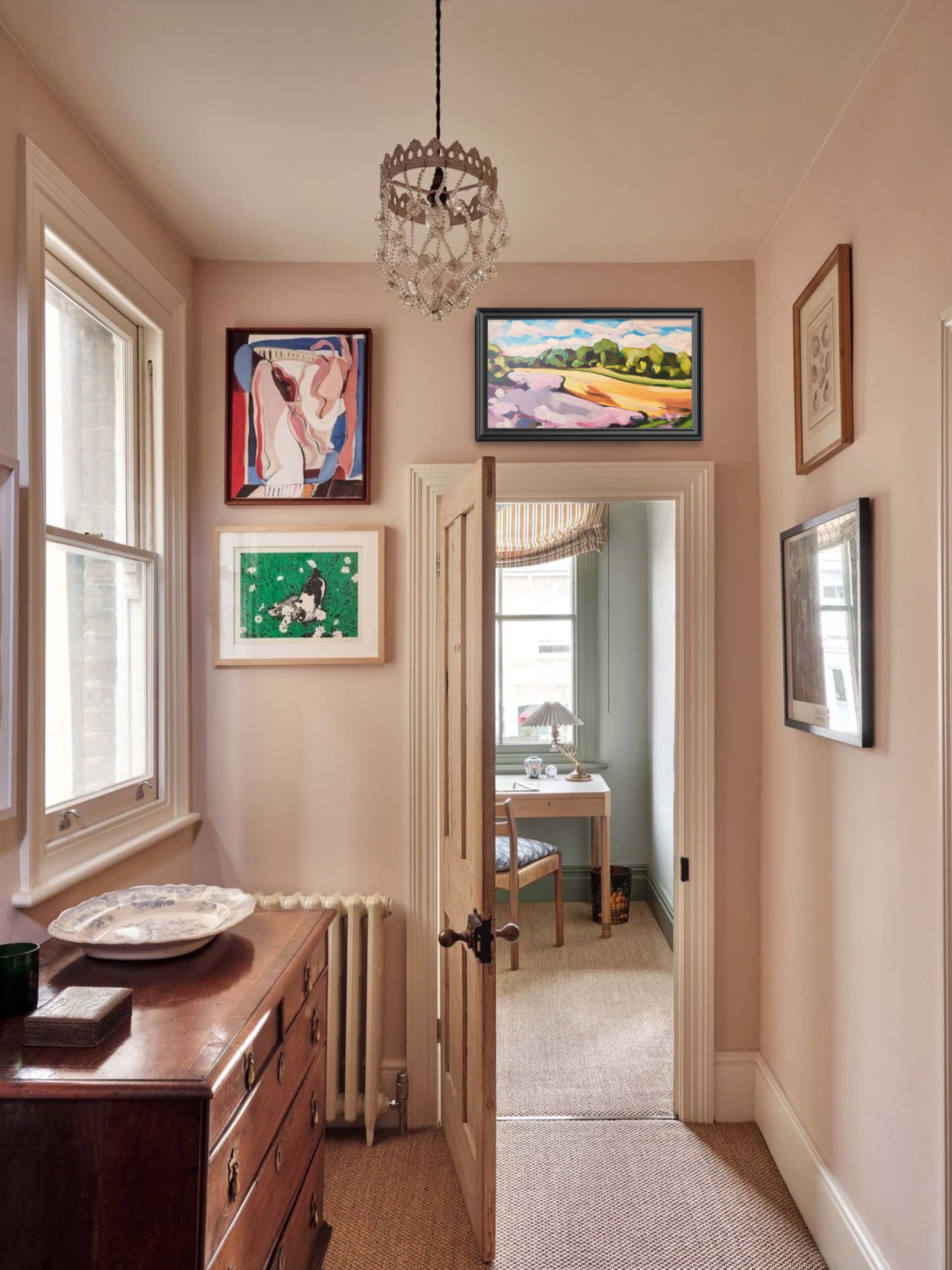 Hallway with framed pictures on the wall, a dresser, and a door leading to another room.