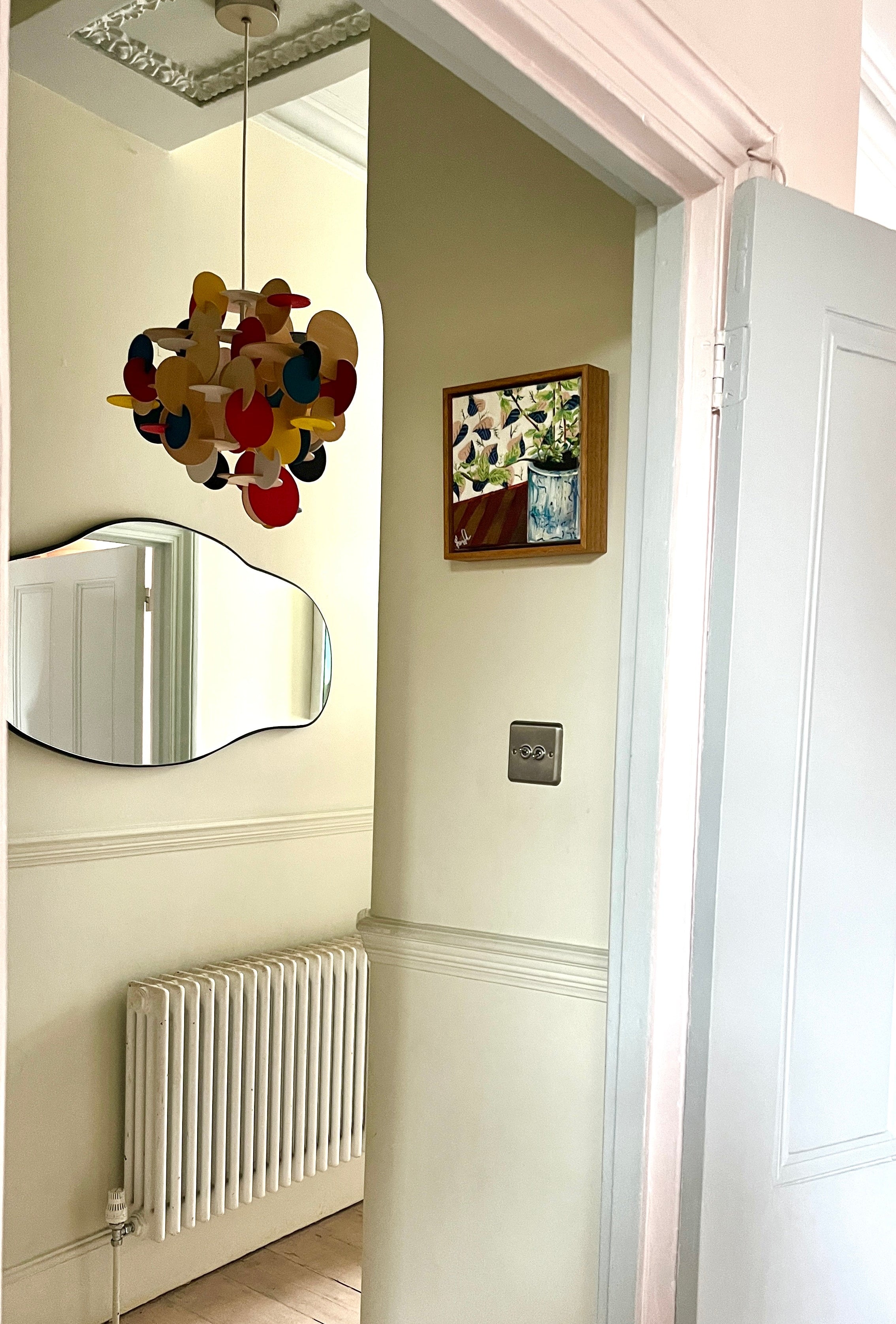 Narrow hallway with a mirror, radiator, and decorative wall art.