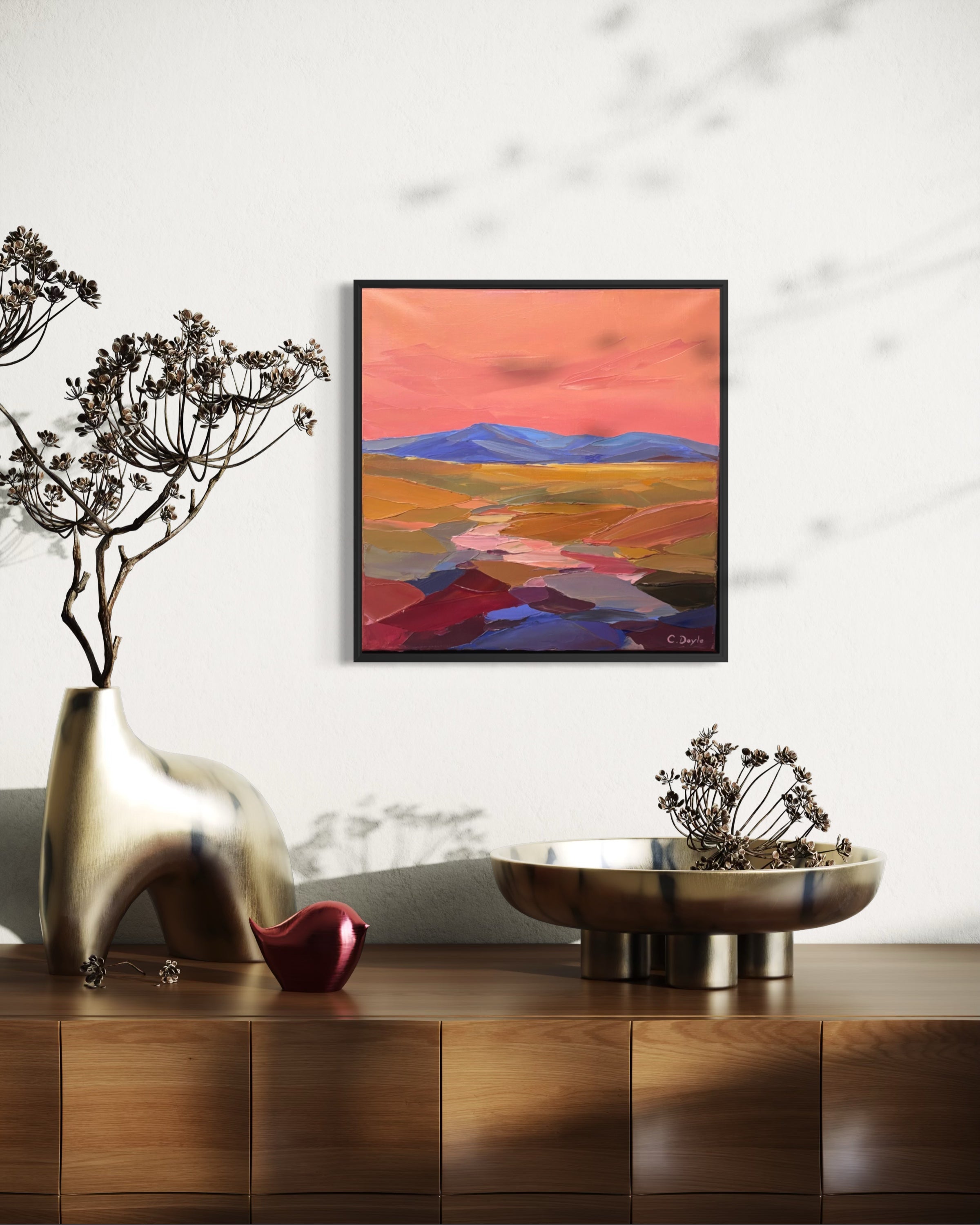 Decorative setup with a gold vase, red object, and metallic bowl on a wooden surface, featuring a colorful abstract painting in the background.