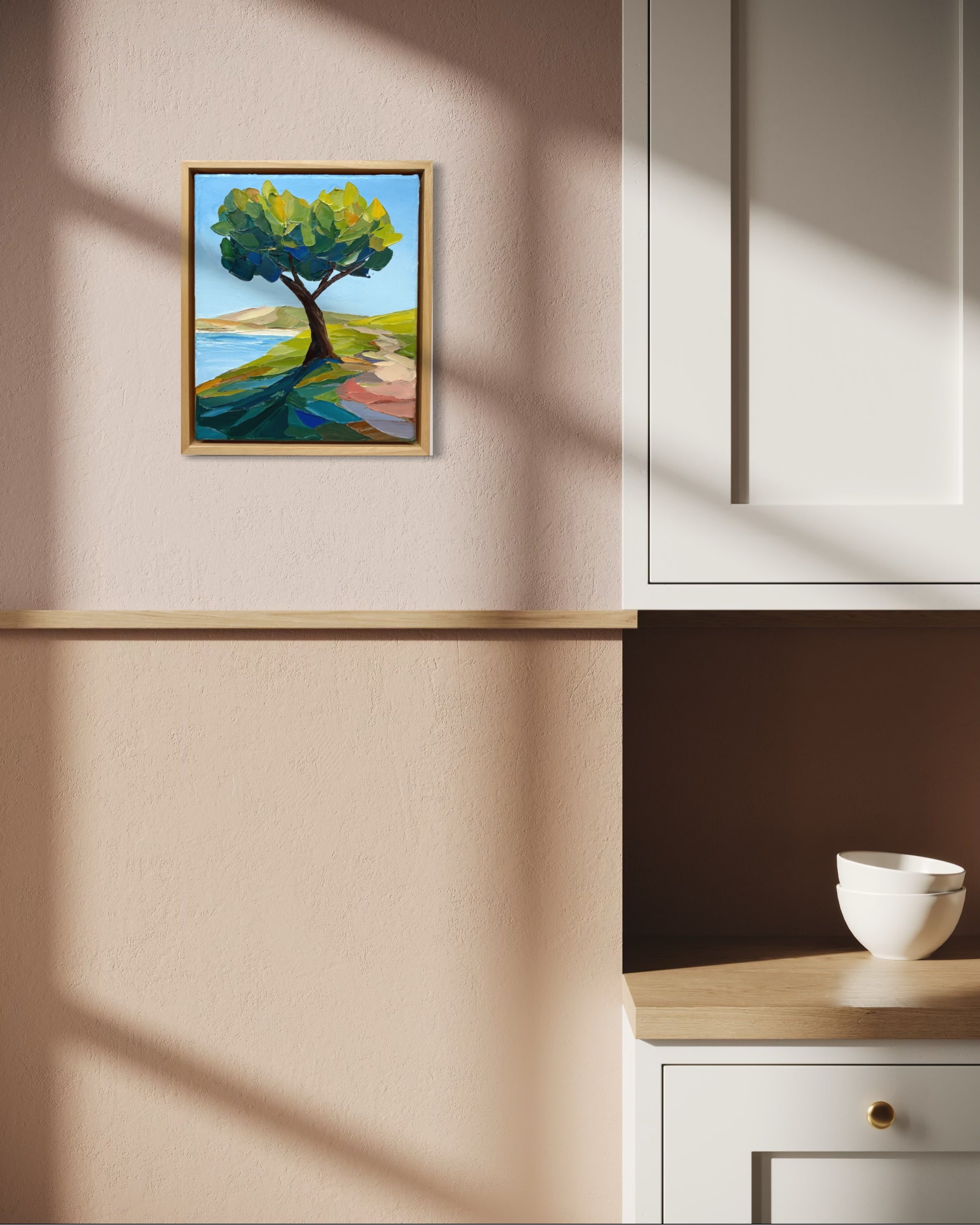 Framed painting of a tree on a wall in a room with a bowl on a surface.