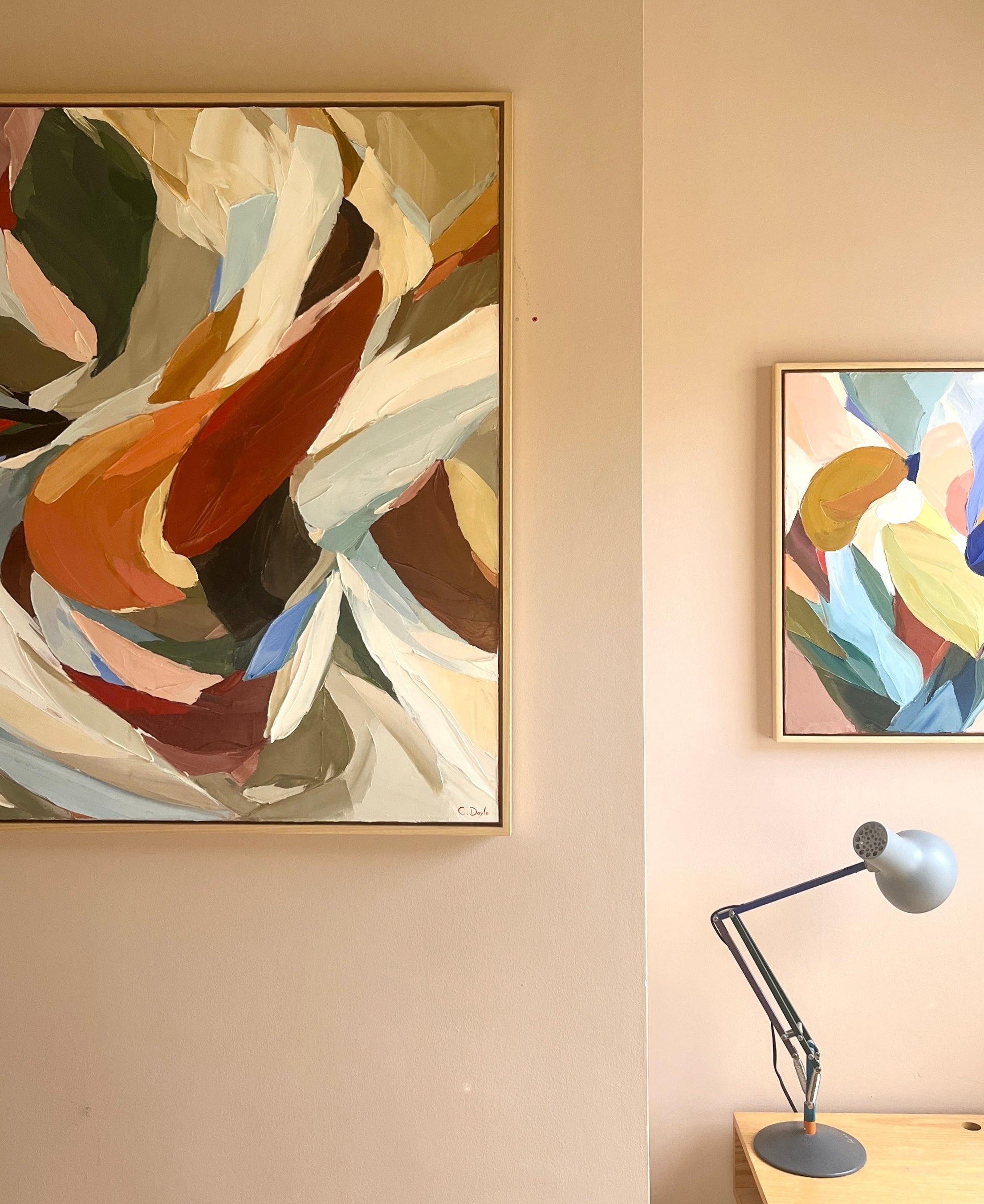 Two abstract artworks on a wall with a lamp on a table below.