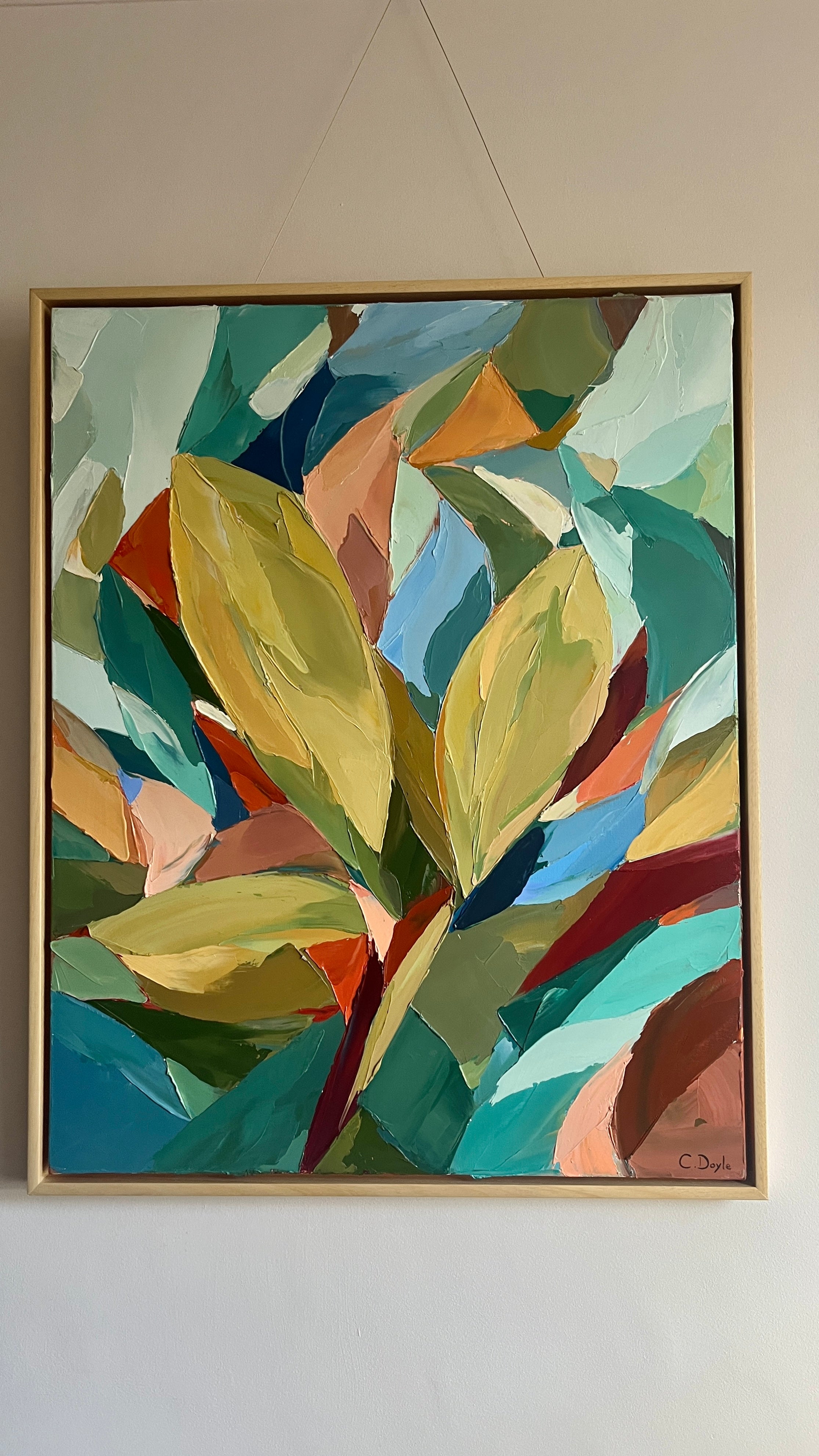 Abstract painting with colorful leaves in a gold frame on a white wall