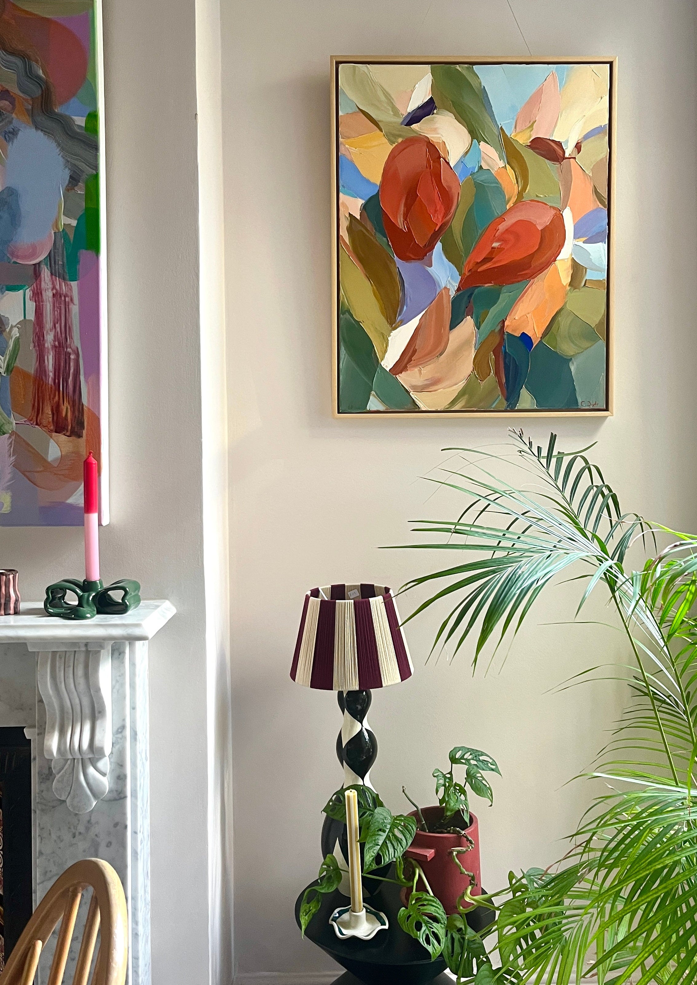 Abstract painting on a wall with a lamp and plants in a room.