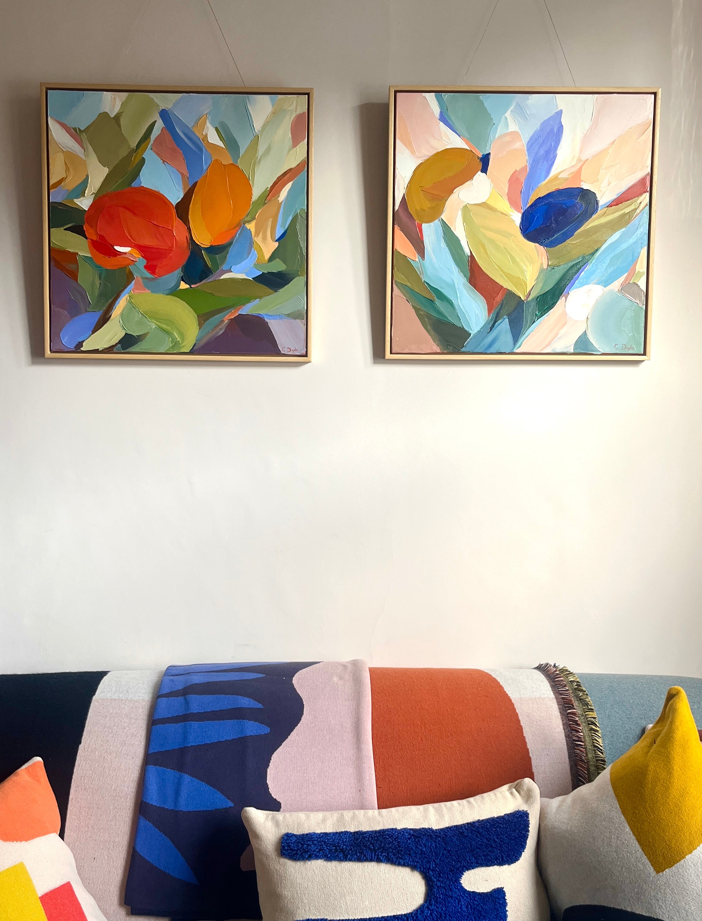 Two abstract paintings on a wall above a colorful sofa with patterned cushions.