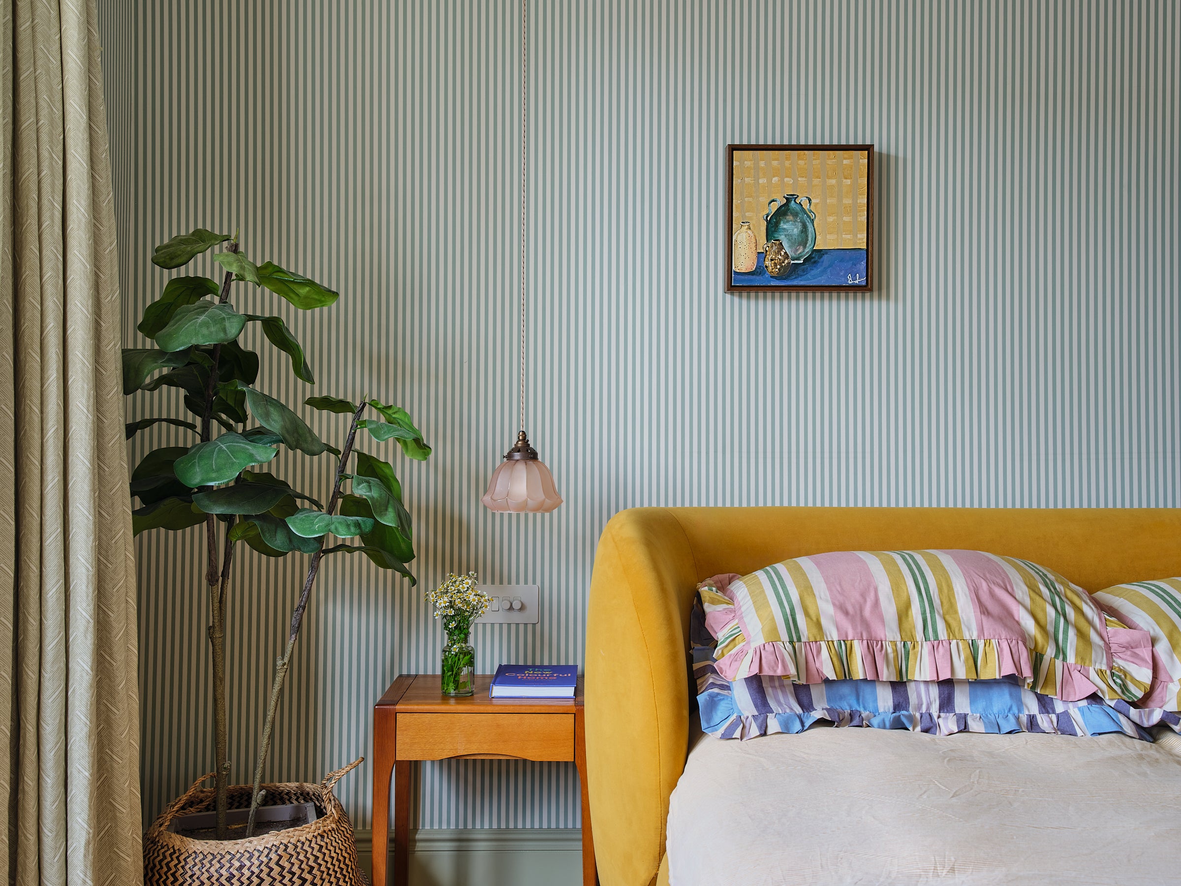 Bedroom scene with small Emma Gurner painting sat above a bed with sripey cushions. 