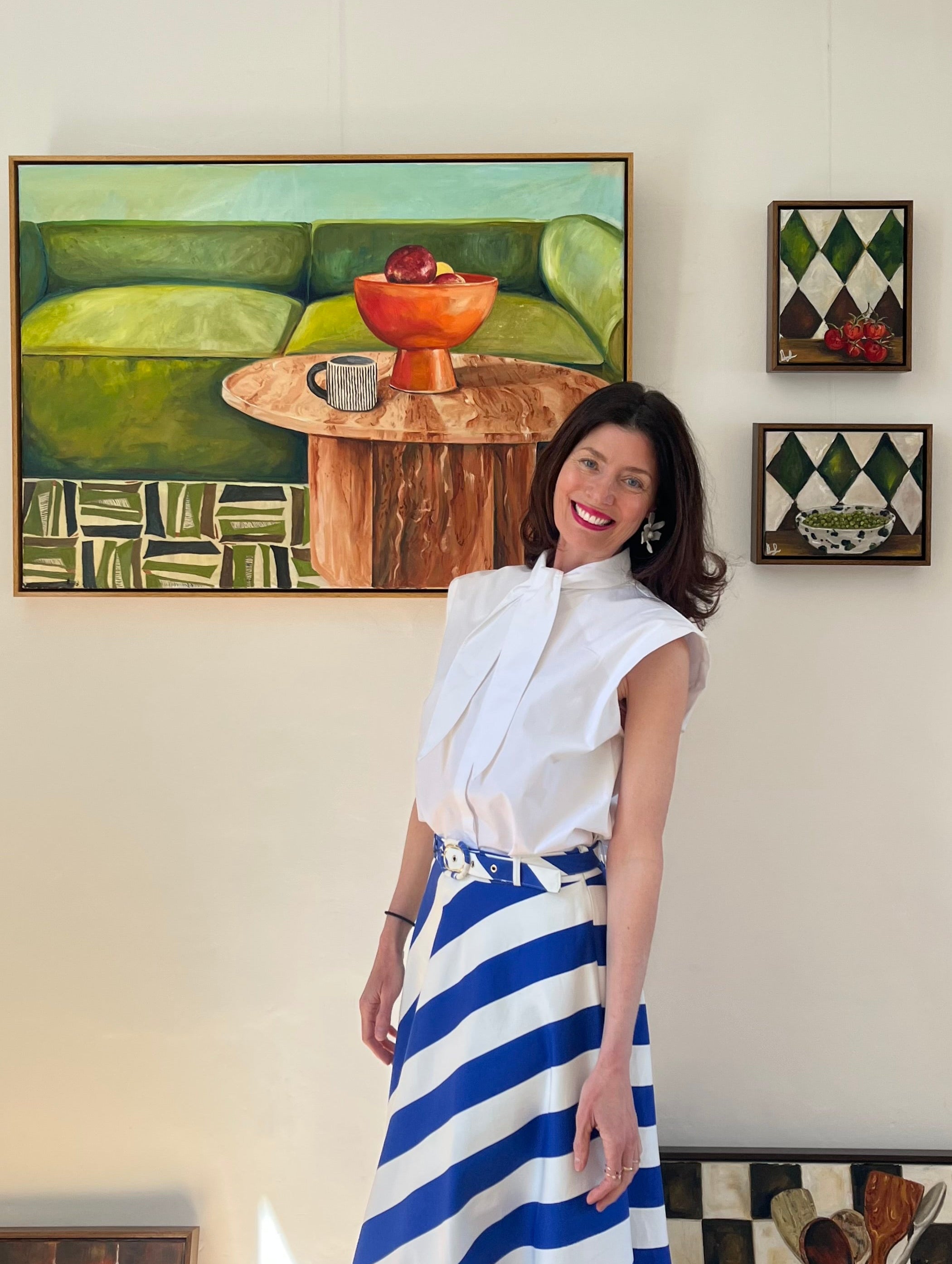 Woman in a white blouse and blue striped skirt standing in a room with wall art.