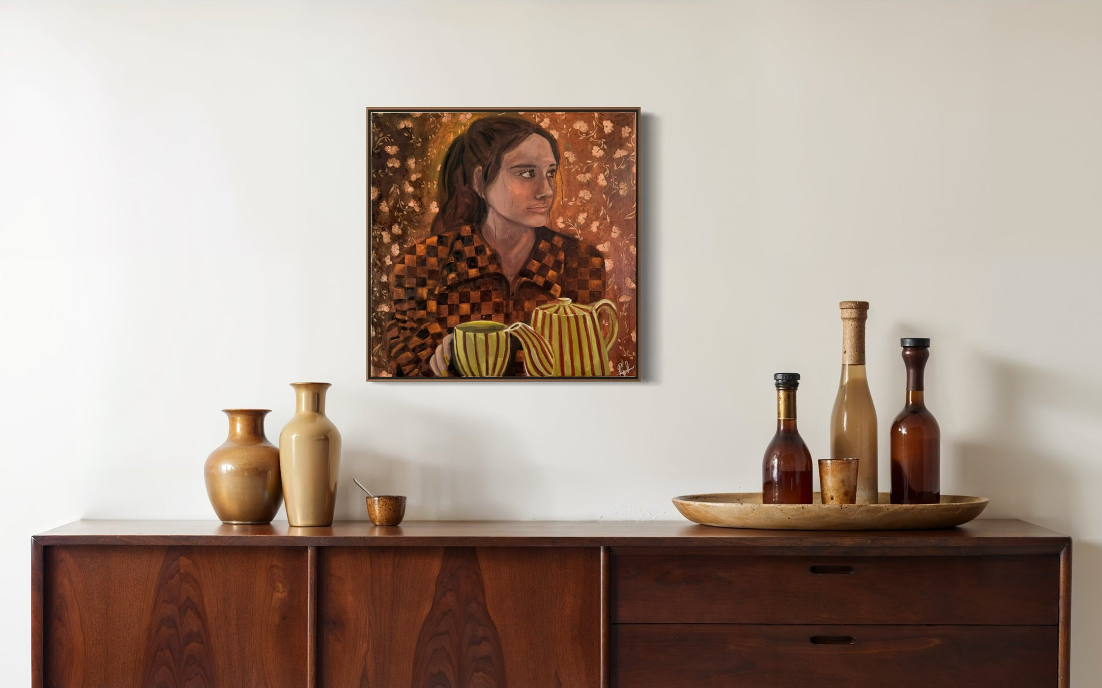 A framed portrait painting of a woman with a striped sweater hangs on a white wall above a dark wood sideboard. The painting features warm brown, gold, and black tones, and the room is styled with decorative vases and bottles on the cabinet.