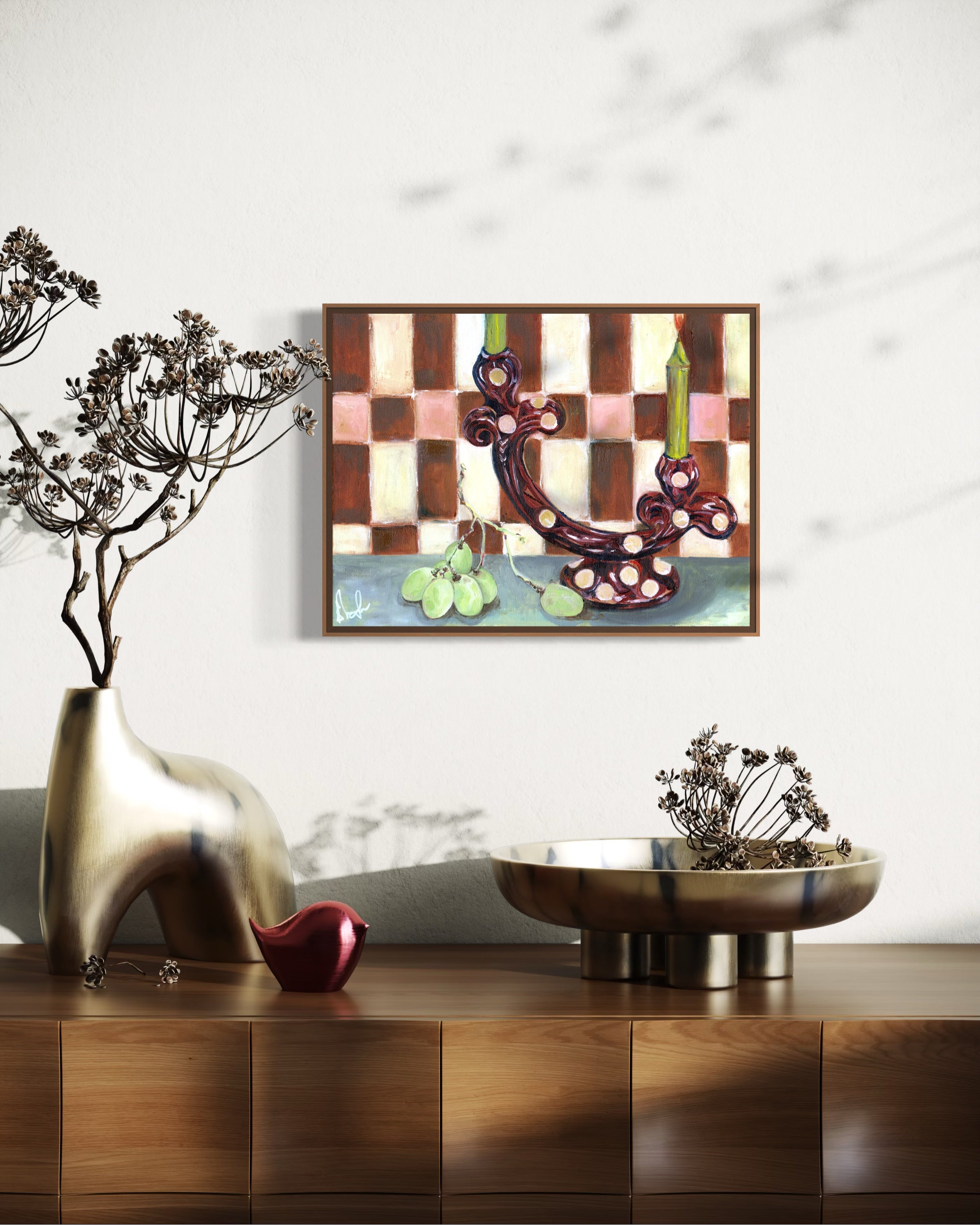 Decorative setup with a gold vase, red apple, bronze bowl, and abstract painting on a white wall.