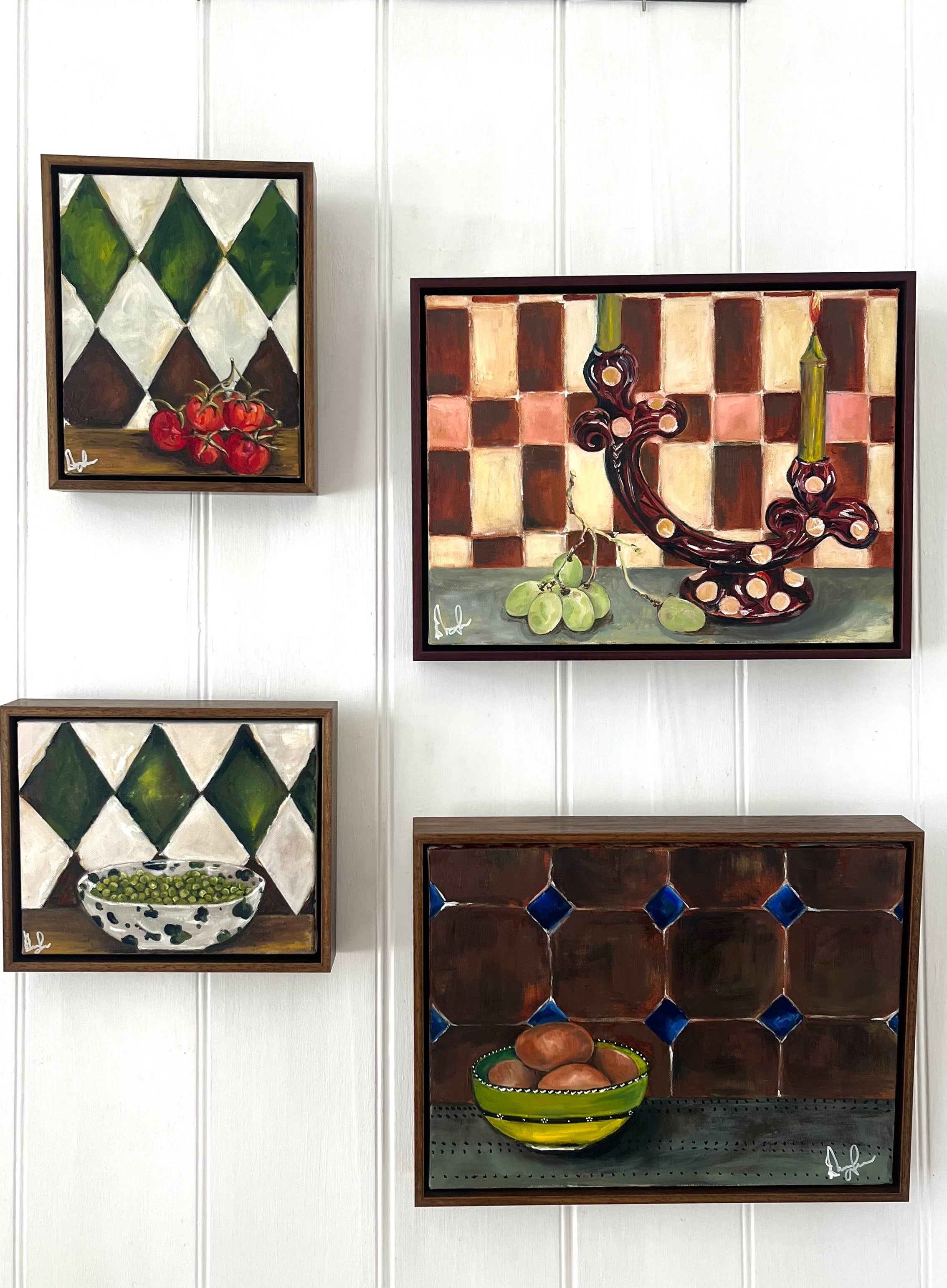Four framed artworks on a white paneled wall