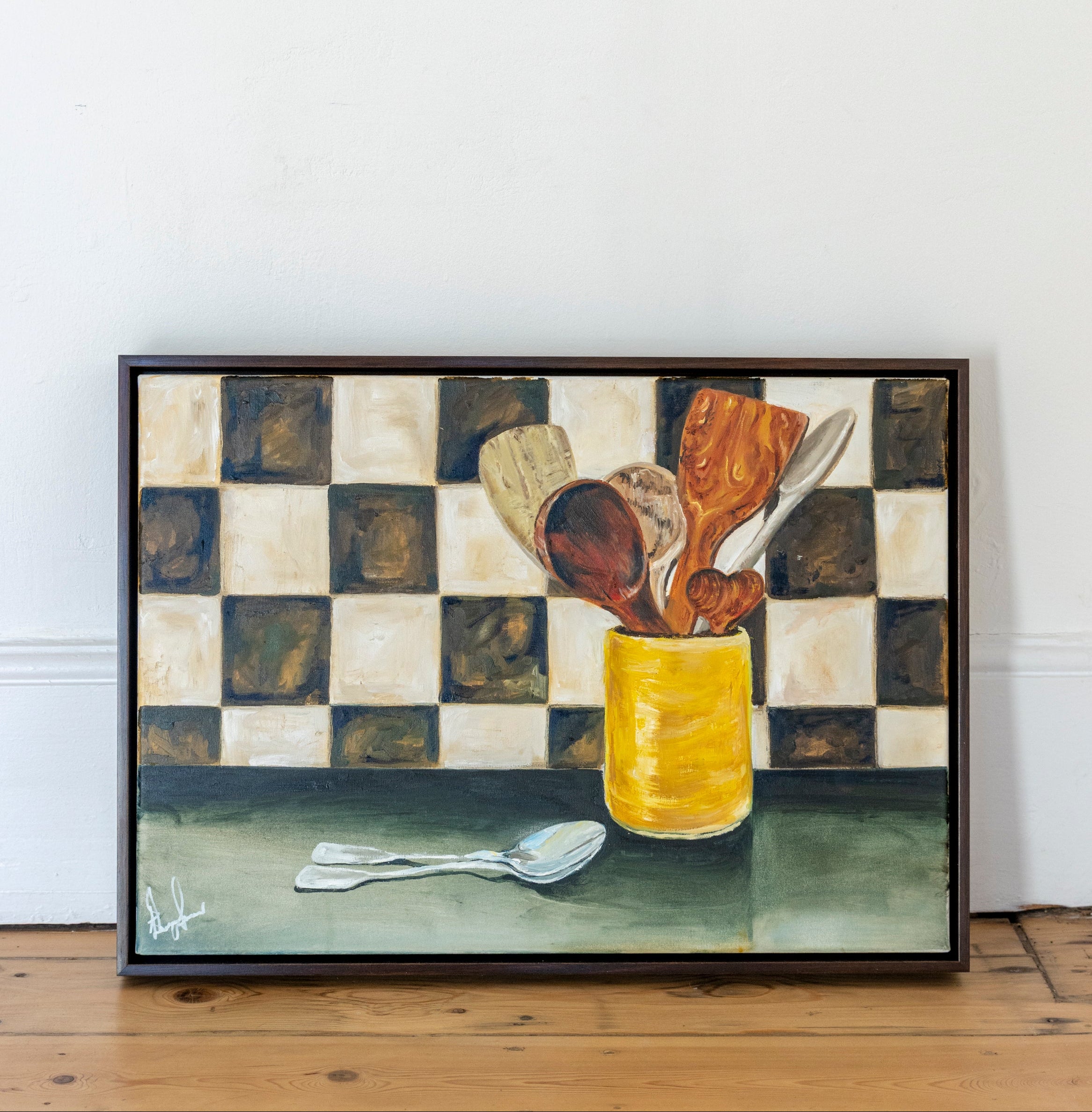 Framed artwork of a still life with a yellow jar and utensils on a checkered surface.