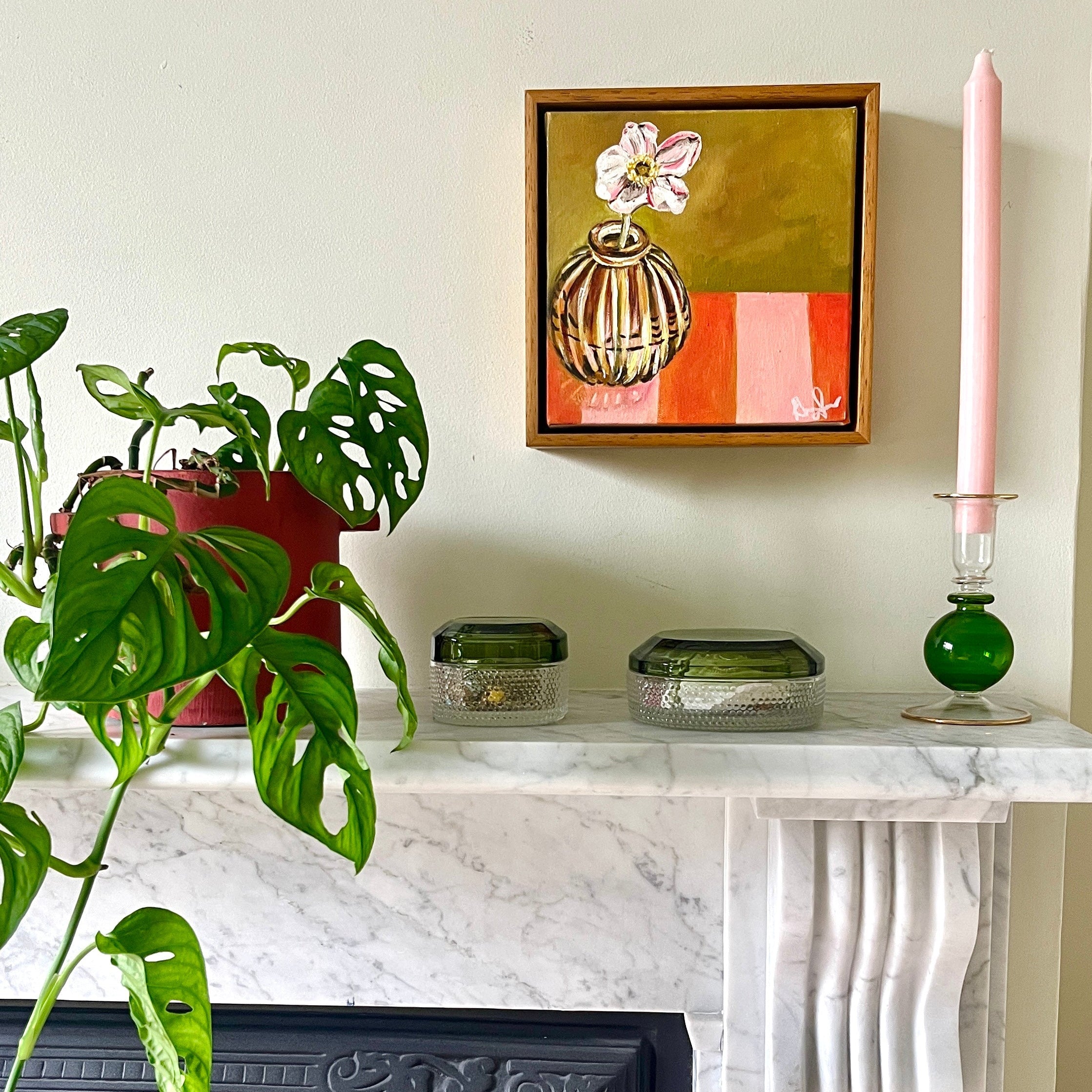 Decorative Marble fireplace  styled with a plant, candle, and framed Emma Gurner artwork set on a light-coloured wall. 