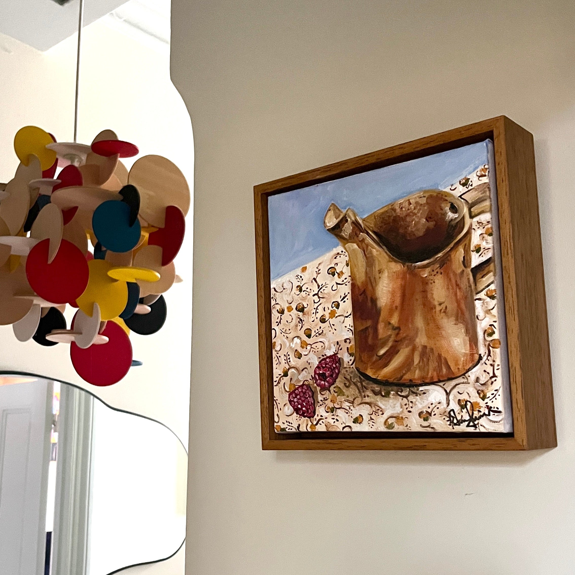 Painting on a wall with a colourful ceiling lamp sitting next to it. 