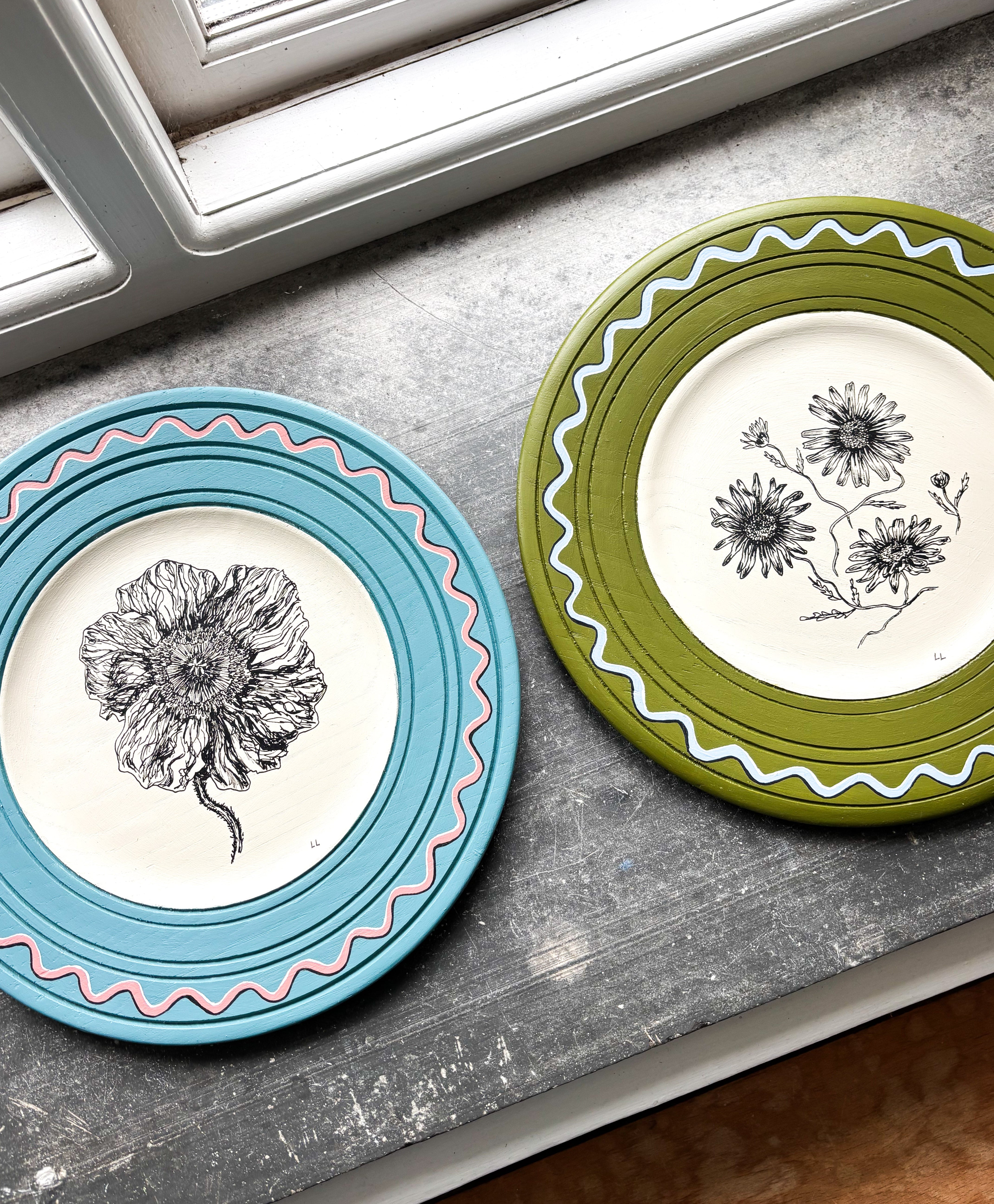 Two decorative plates with floral designs on a surface near a window.