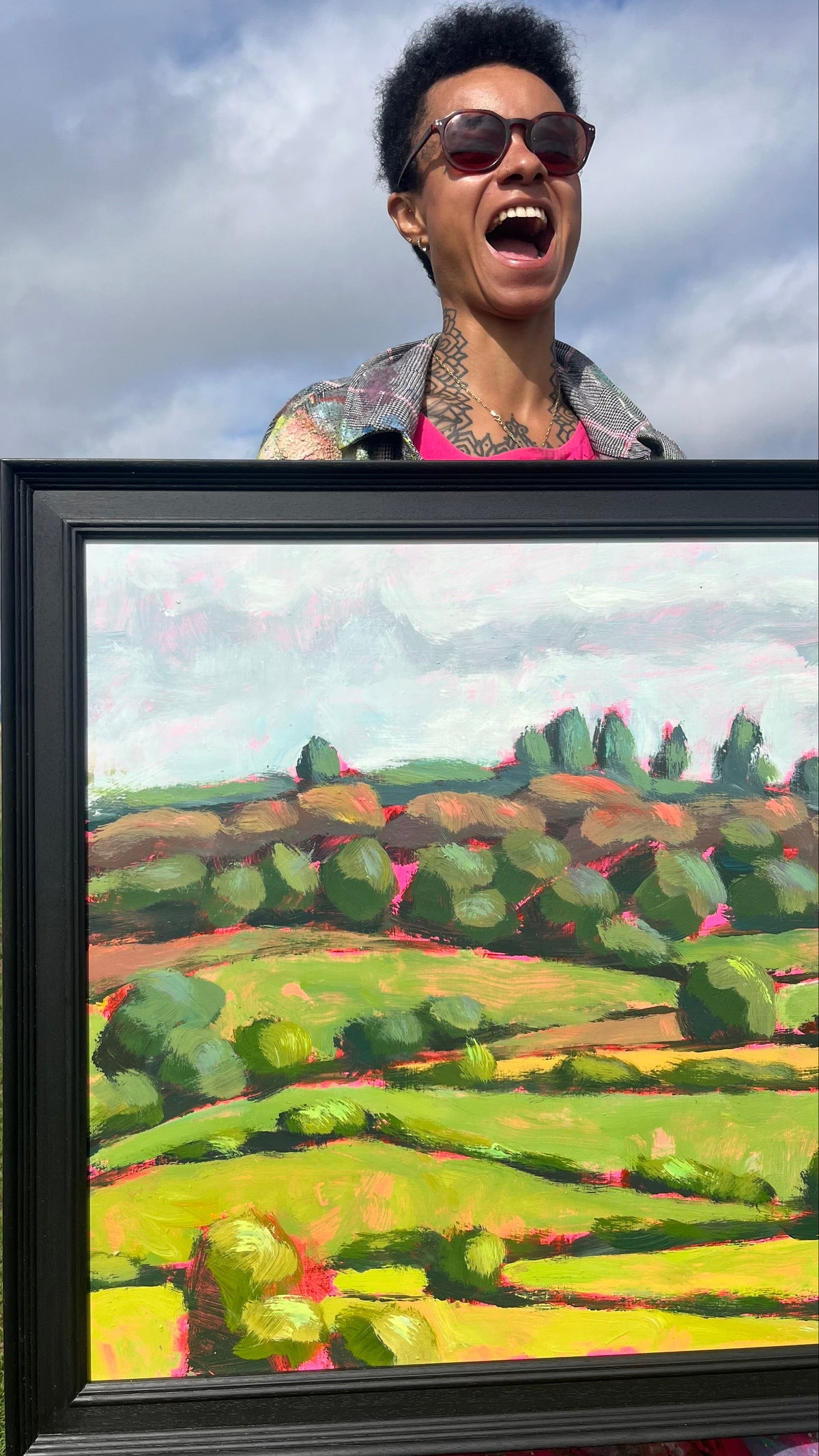 Artist holding landscape art with blue sky behind. 