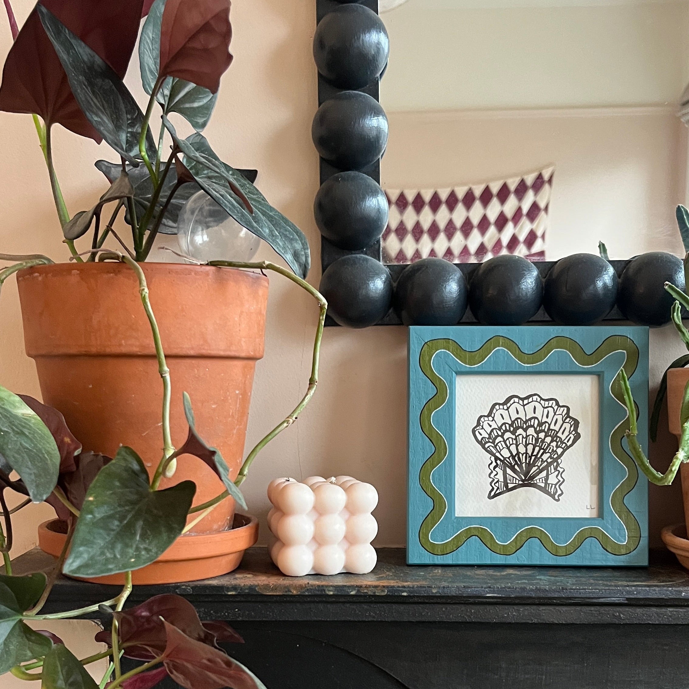 Decorative mantel with plants, candles, and a framed picture on a fireplace.