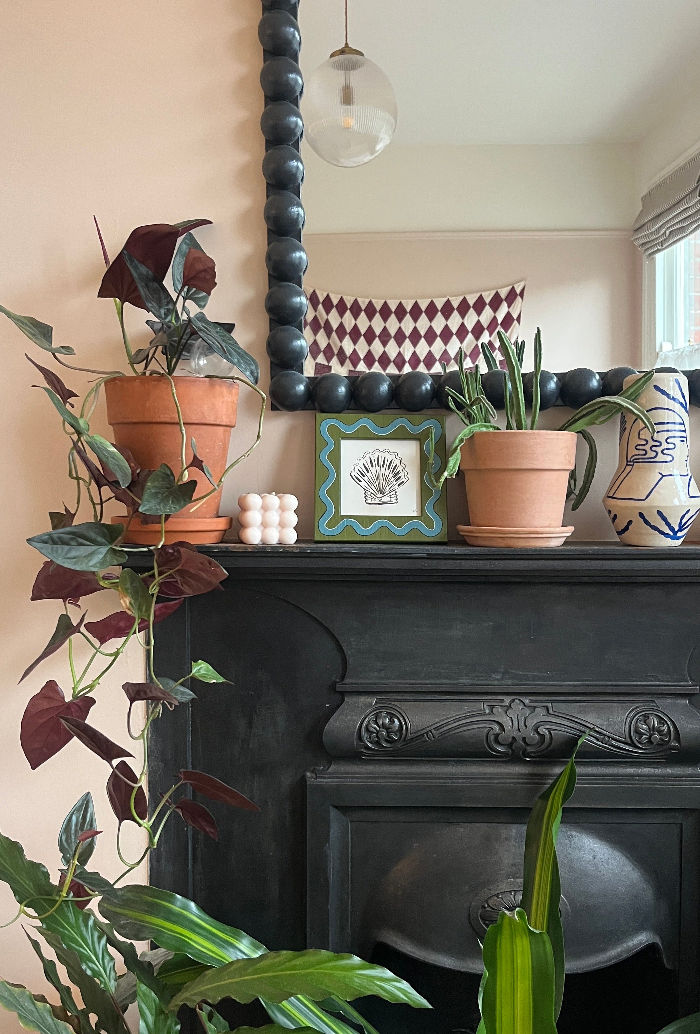 Decorative mantelpiece with plants, a clock, and a mirror above a fireplace.