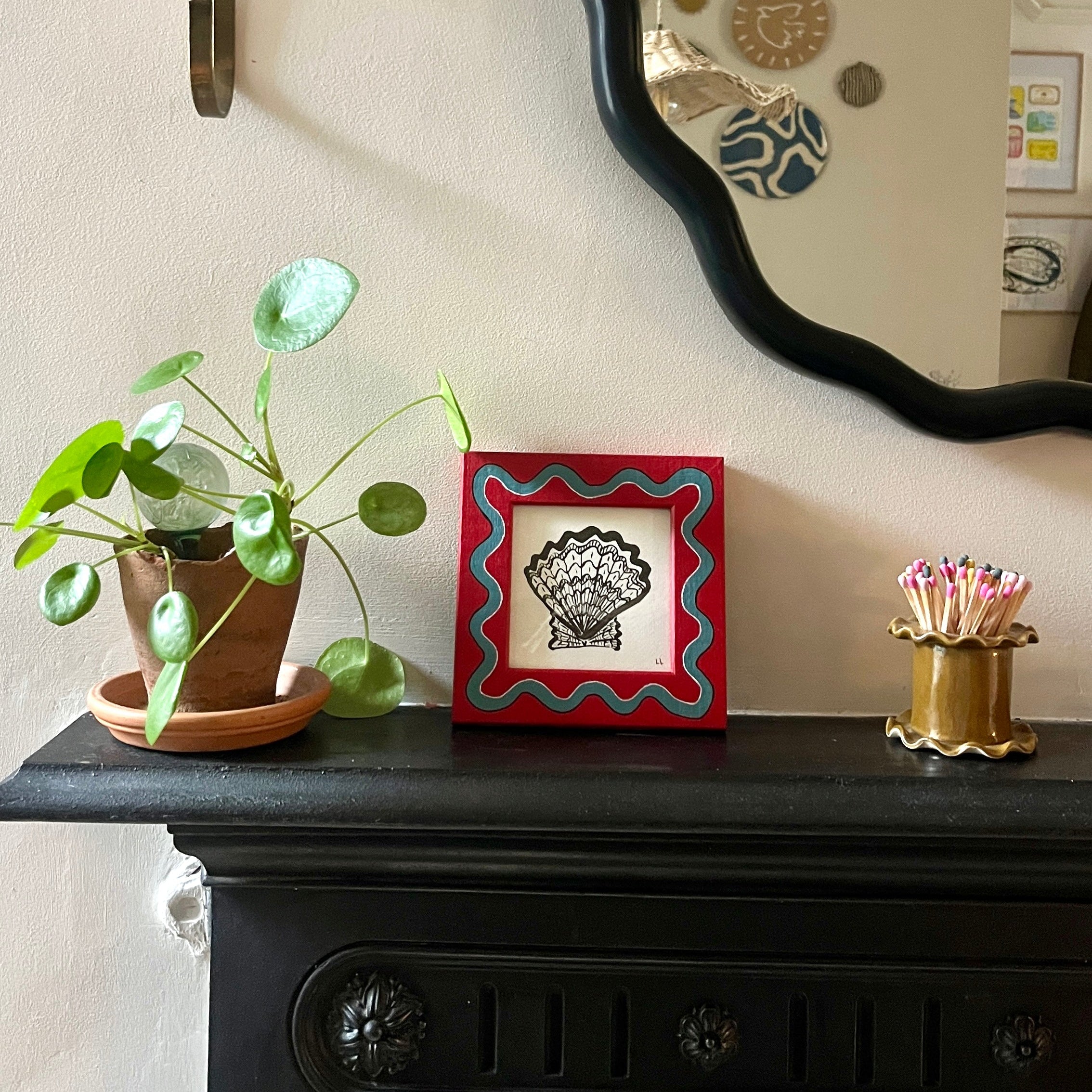 Decorative items on a mantelpiece including a plant, framed picture, and candles.
