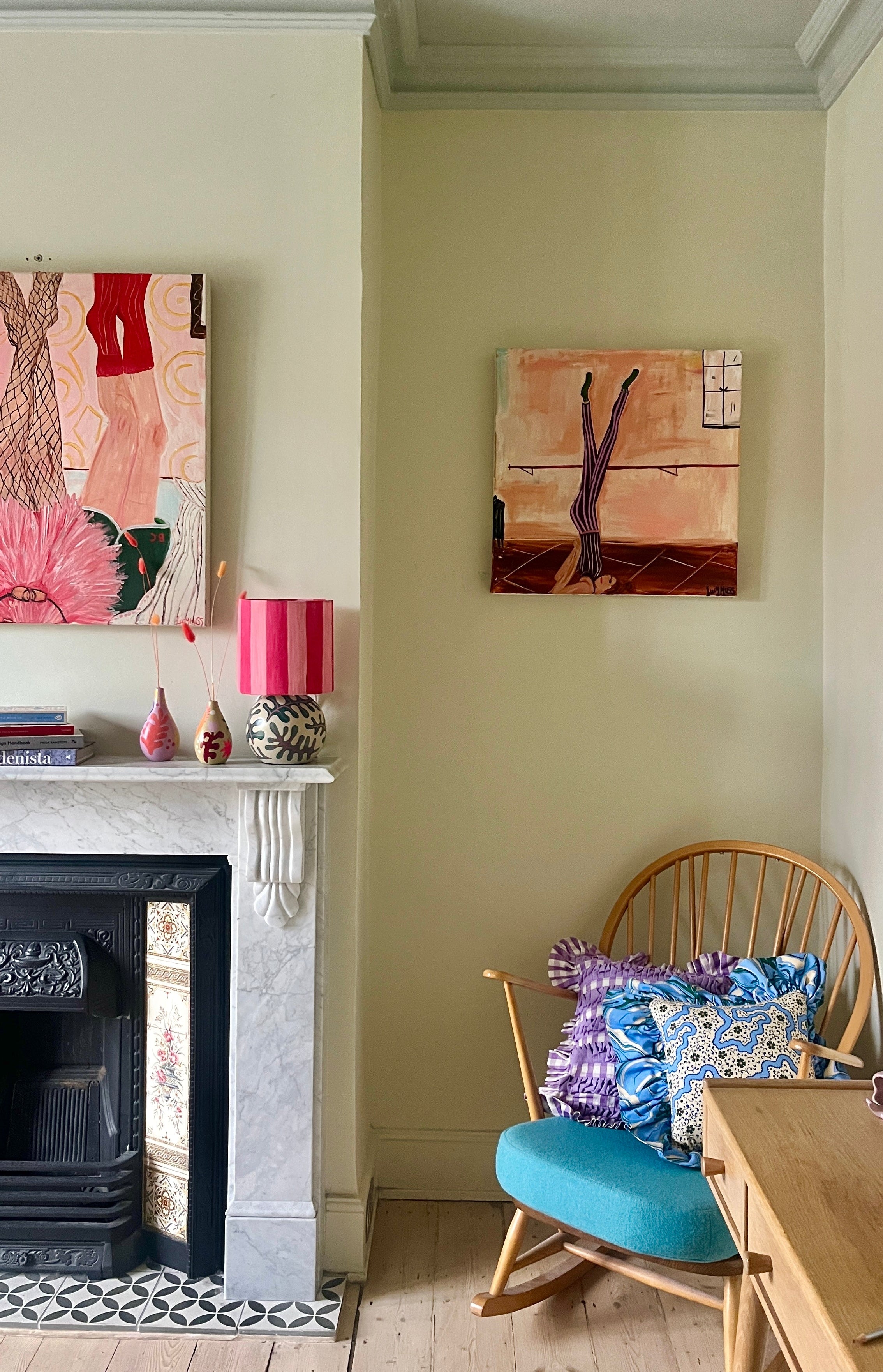 Image of painting above a rocking chair next to a fireplace. 